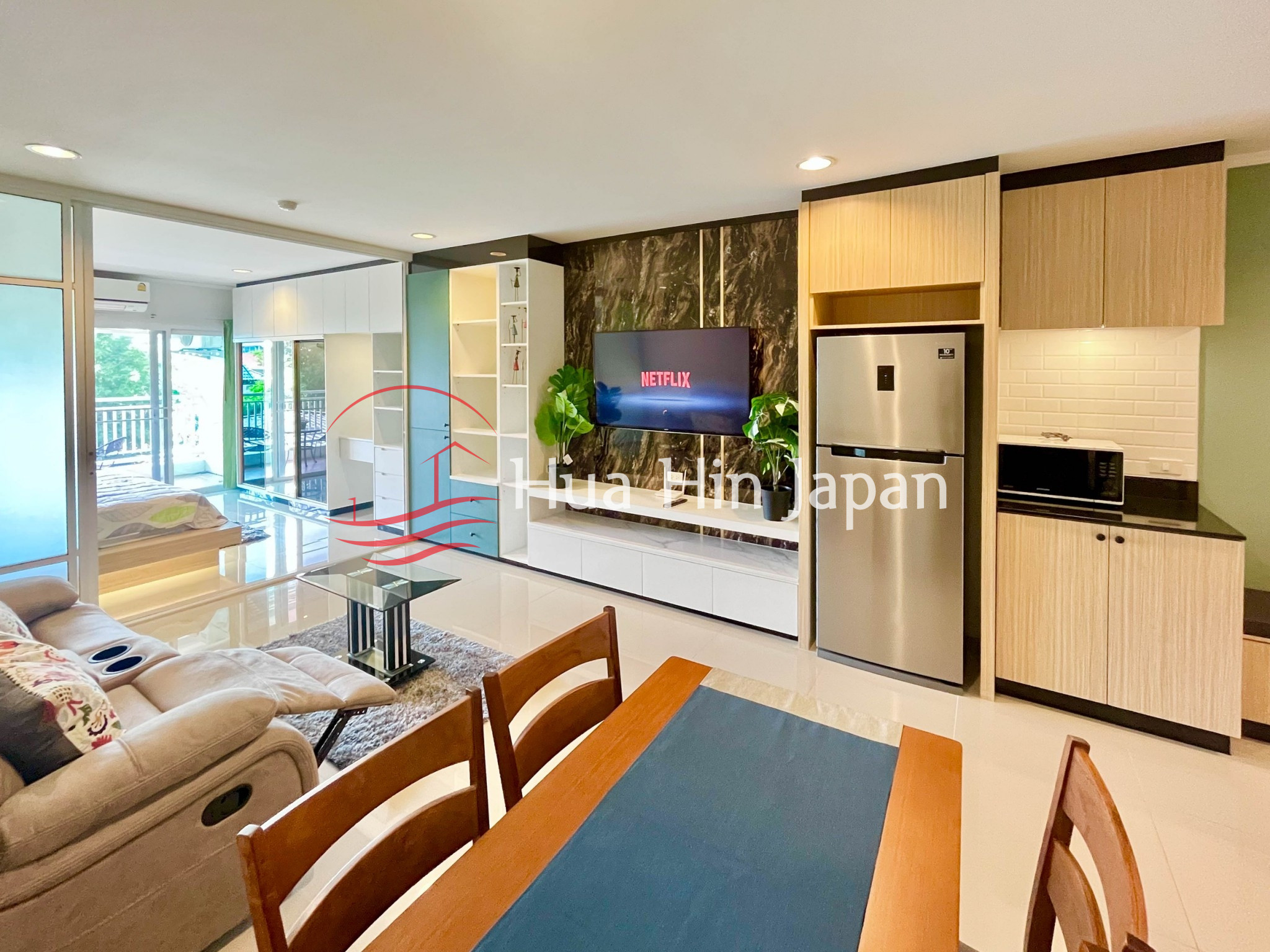 Modern apartment kitchen and living area with wooden cabinets, TV, and dining space