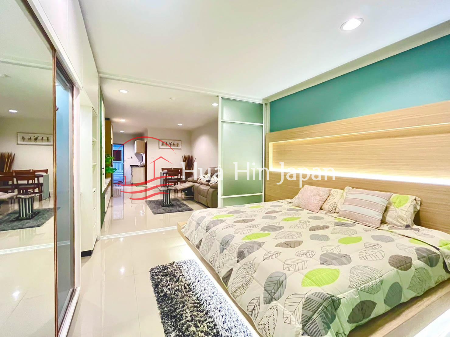 Modern bedroom with green accent wall, bed, large wardrobe, and natural light