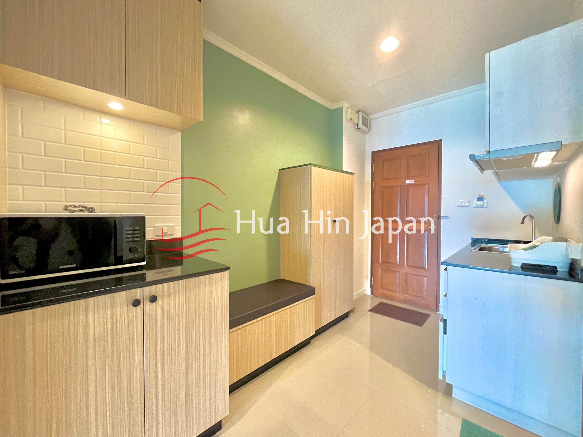 Modern apartment kitchen with wooden cabinets, microwave, sink, and green accent wall