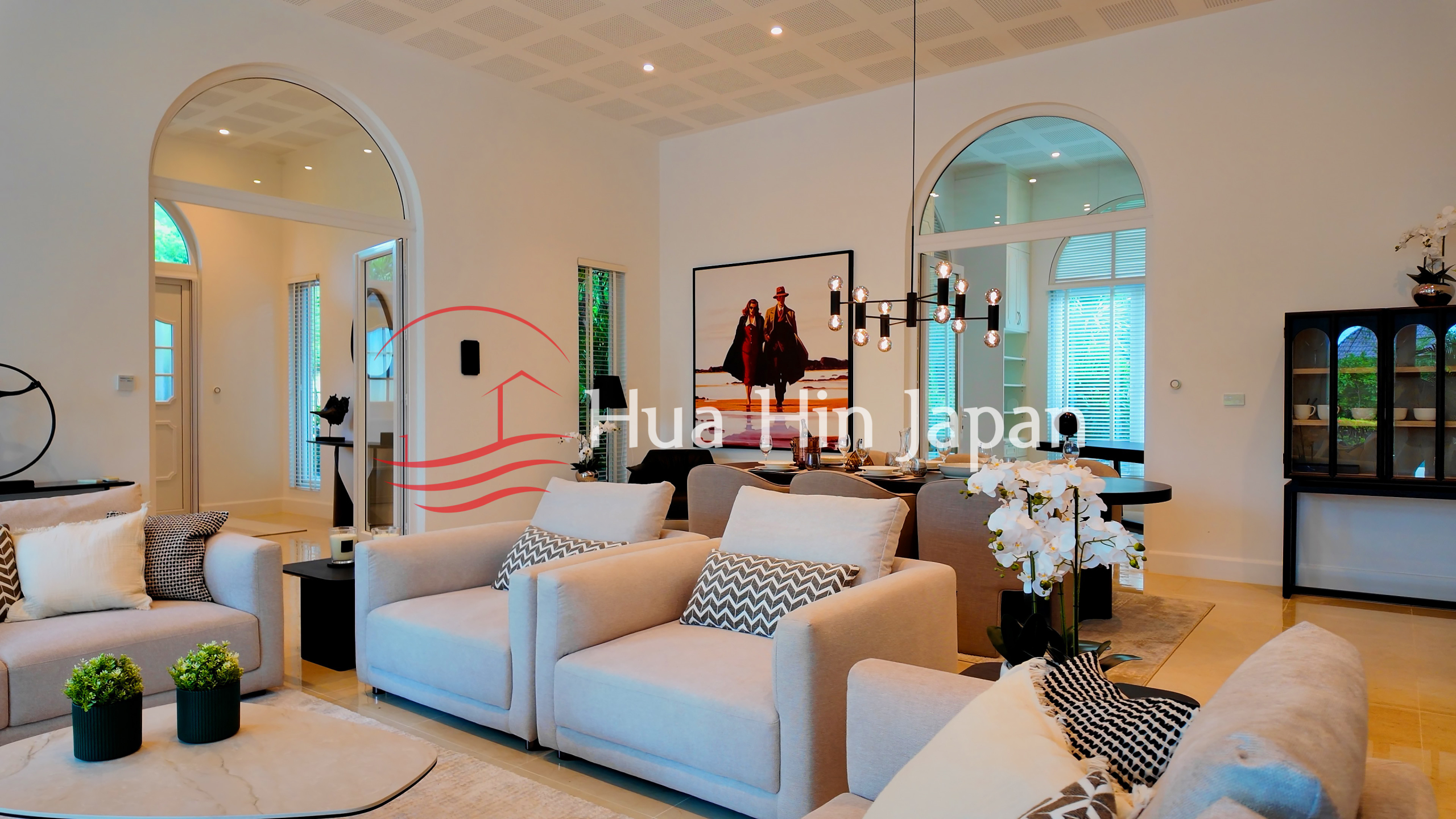 Elegant luxury living room with cream sofas, patterned cushions, modern chandelier, artwork, and arched windows