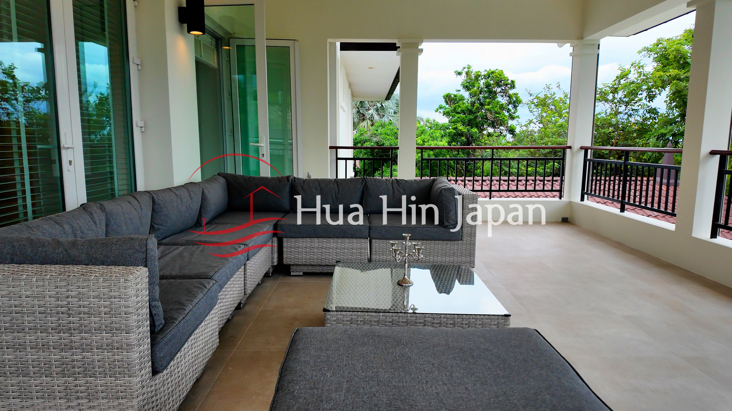 Spacious covered outdoor terrace with a large sectional sofa, glass coffee table, and lush garden views