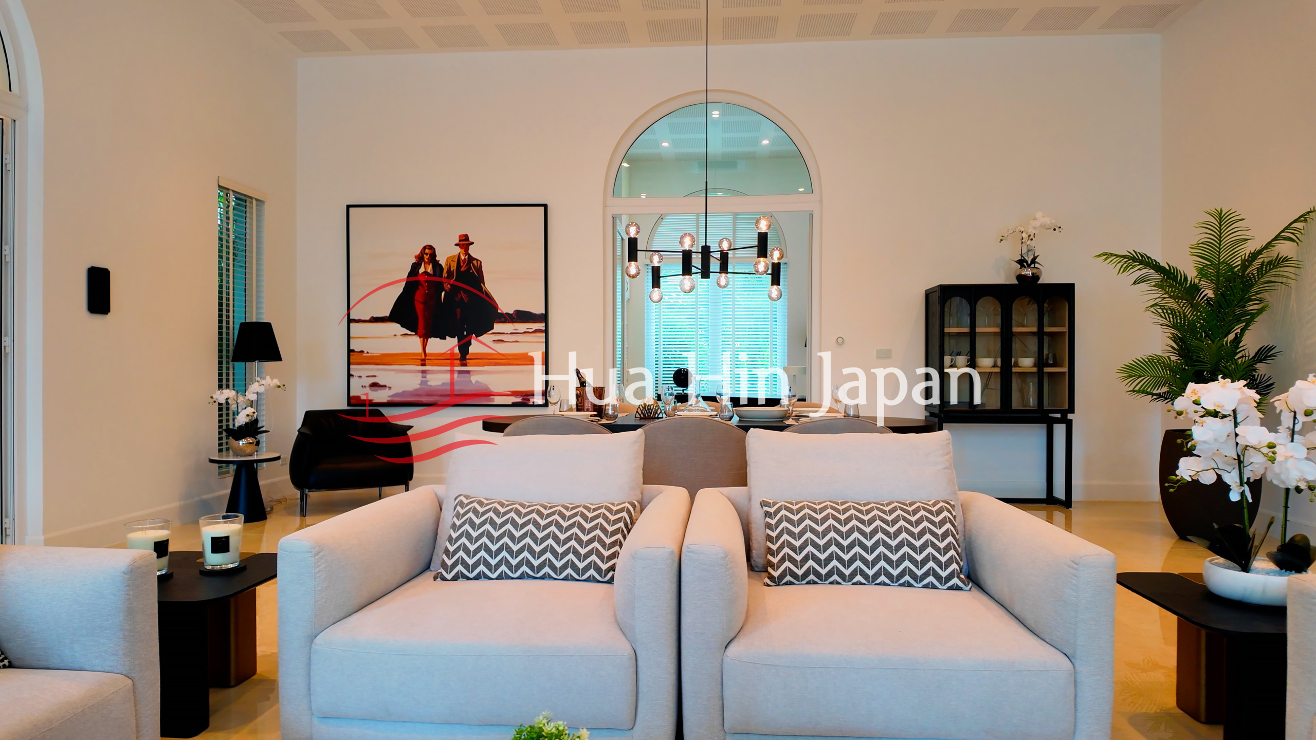 Elegant modern living room with two cream armchairs, decorative cushions, artwork, indoor plants, and stylish lighting