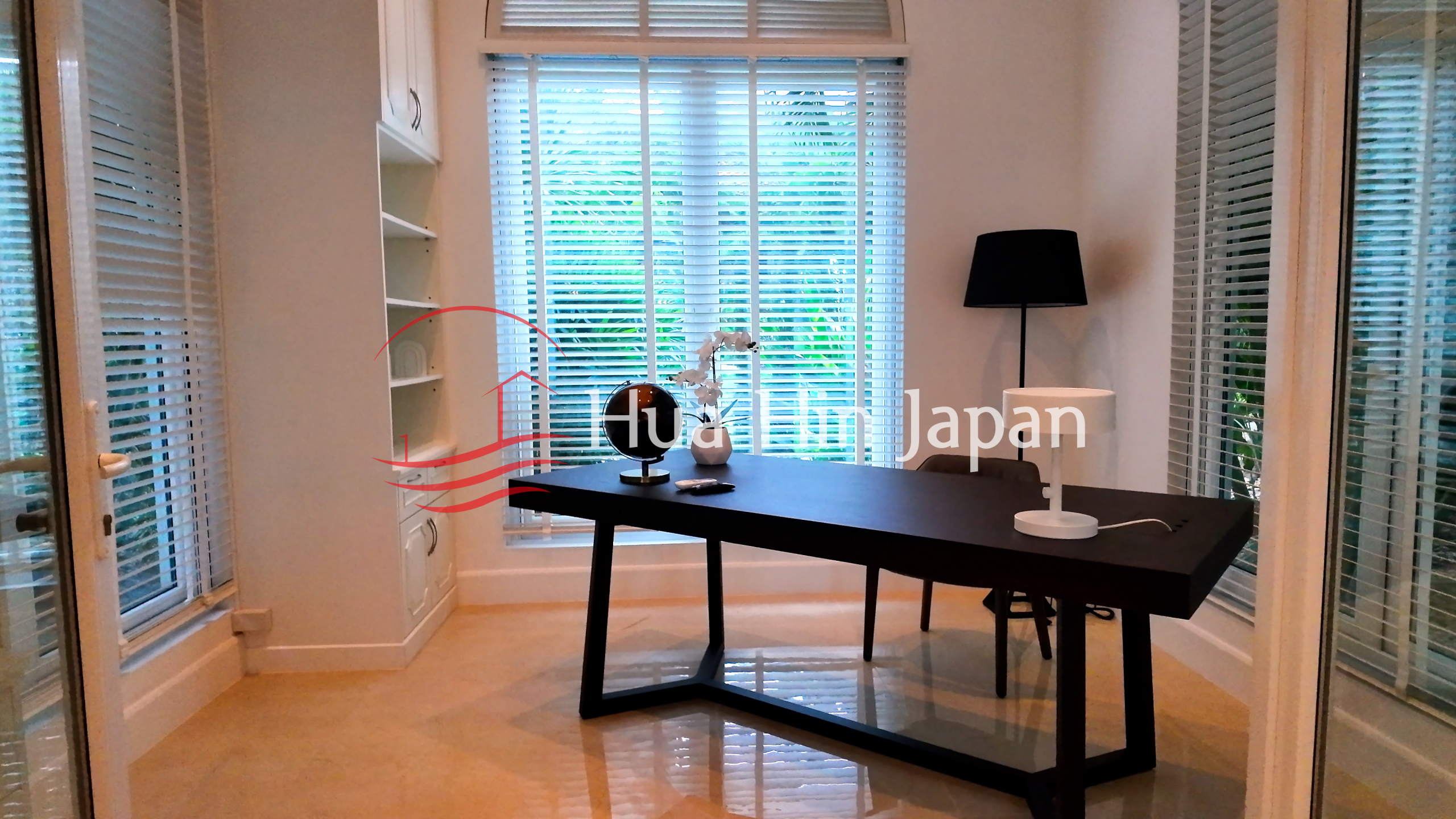 Elegant home office with a black desk, floor lamp, built-in shelves, and large windows with white blinds