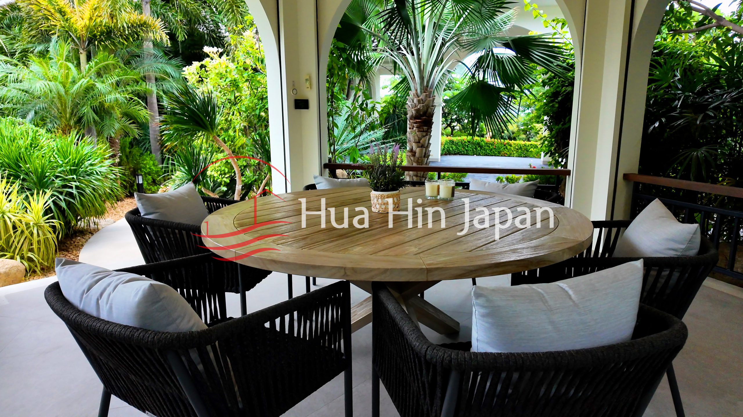Covered outdoor dining area with a round wooden table, comfortable chairs, and lush tropical garden views