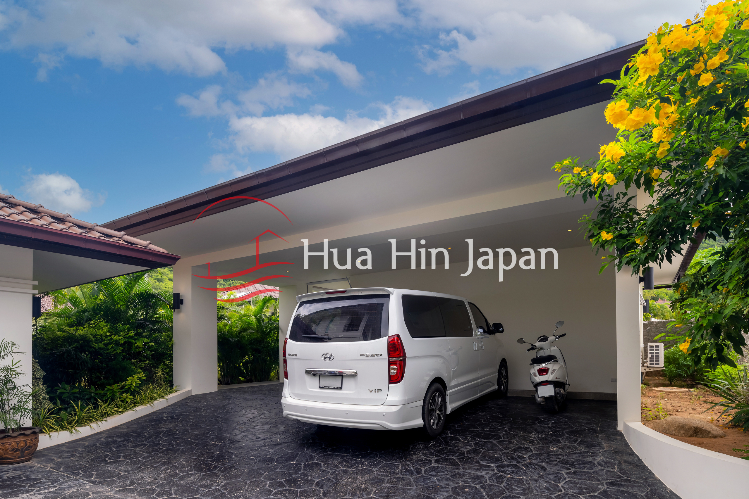 Covered carport with a white van and scooter, surrounded by lush tropical landscaping.
