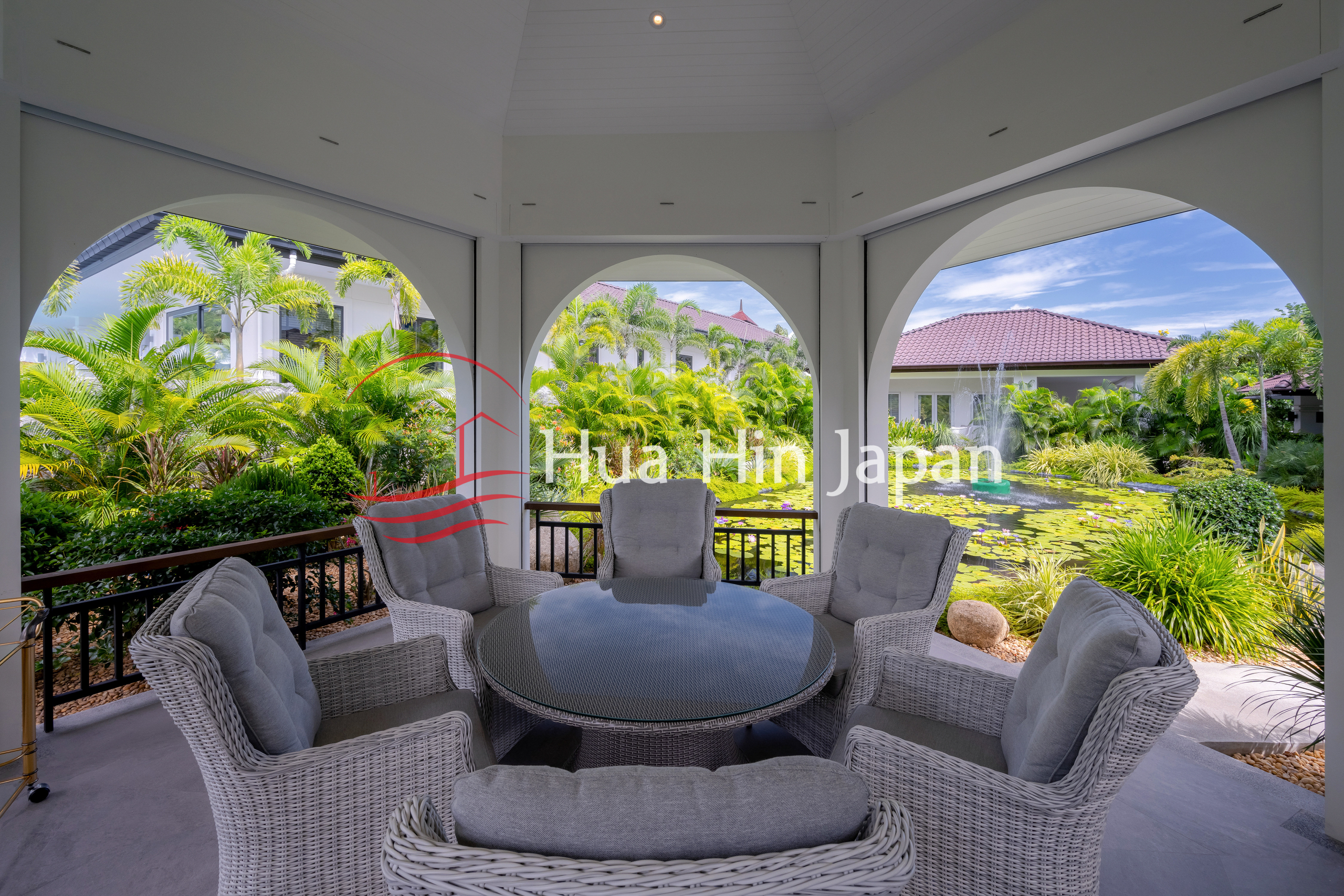 Covered outdoor patio with wicker seating overlooking a lush tropical garden