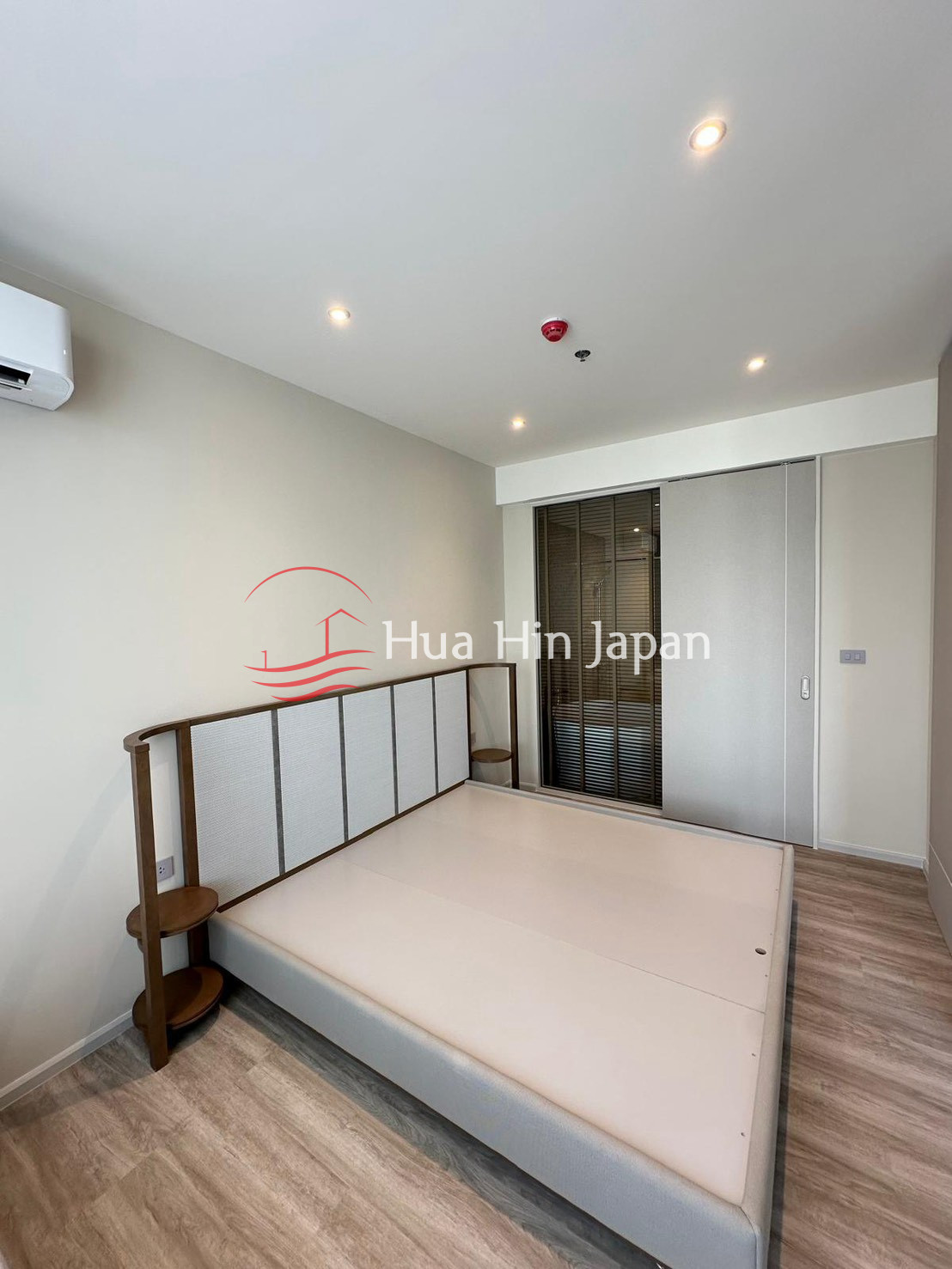 Modern bedroom with a large bed, wooden flooring, air conditioner, and built-in wardrobe