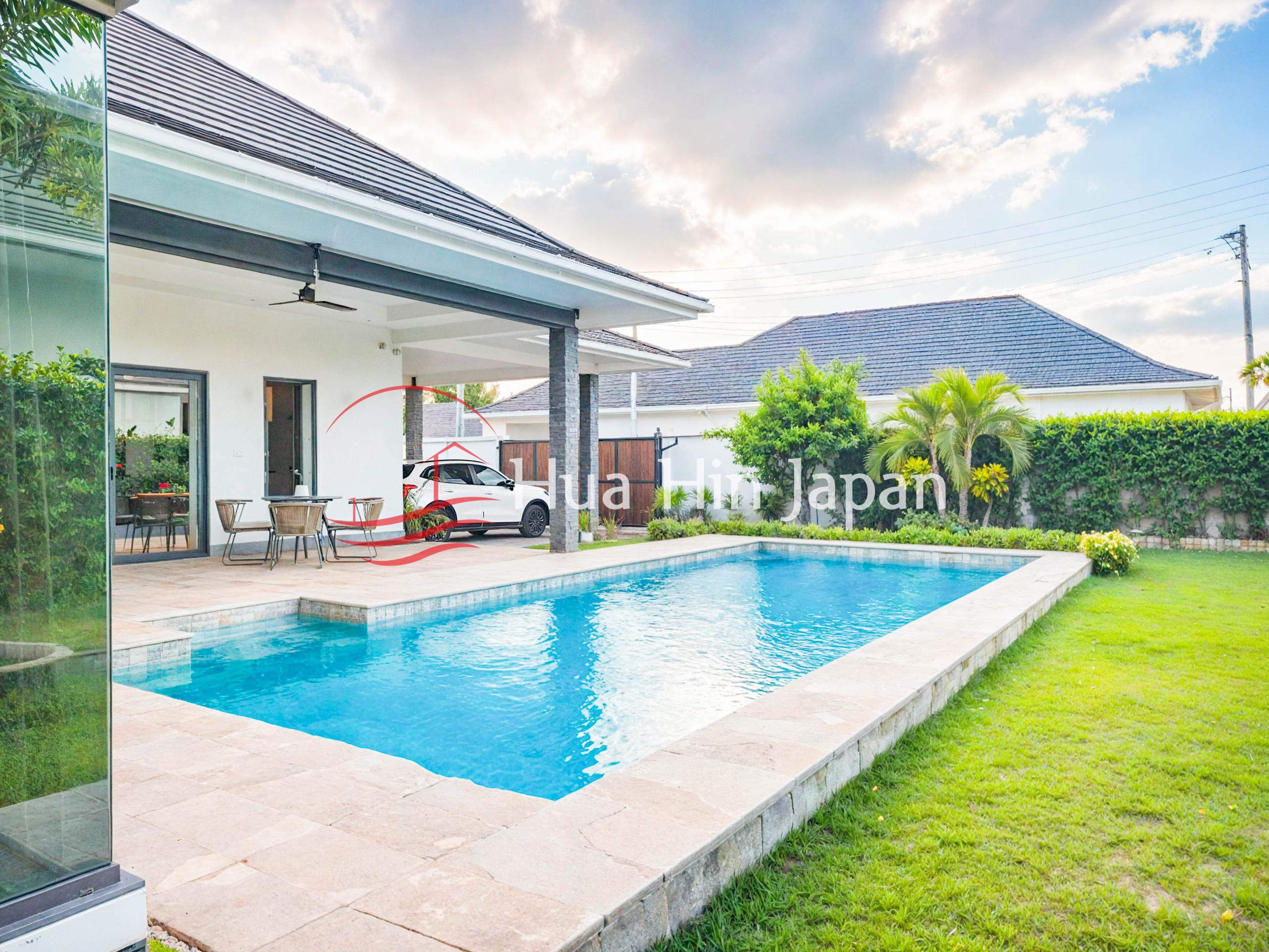 Modern white villa with a private swimming pool, covered patio, landscaped lawn, and tropical plants
