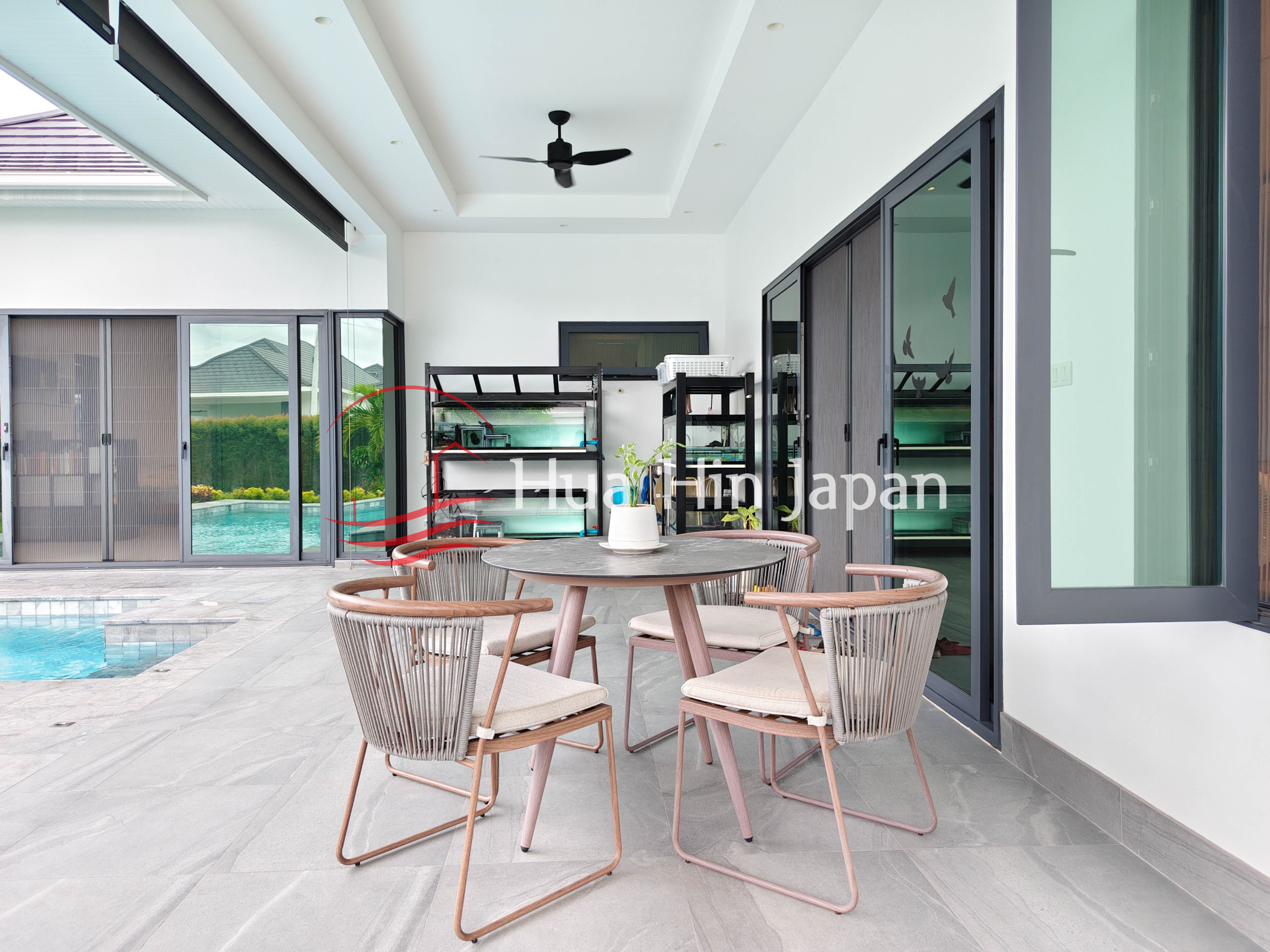 Covered outdoor patio with dining table and four chairs beside a swimming pool