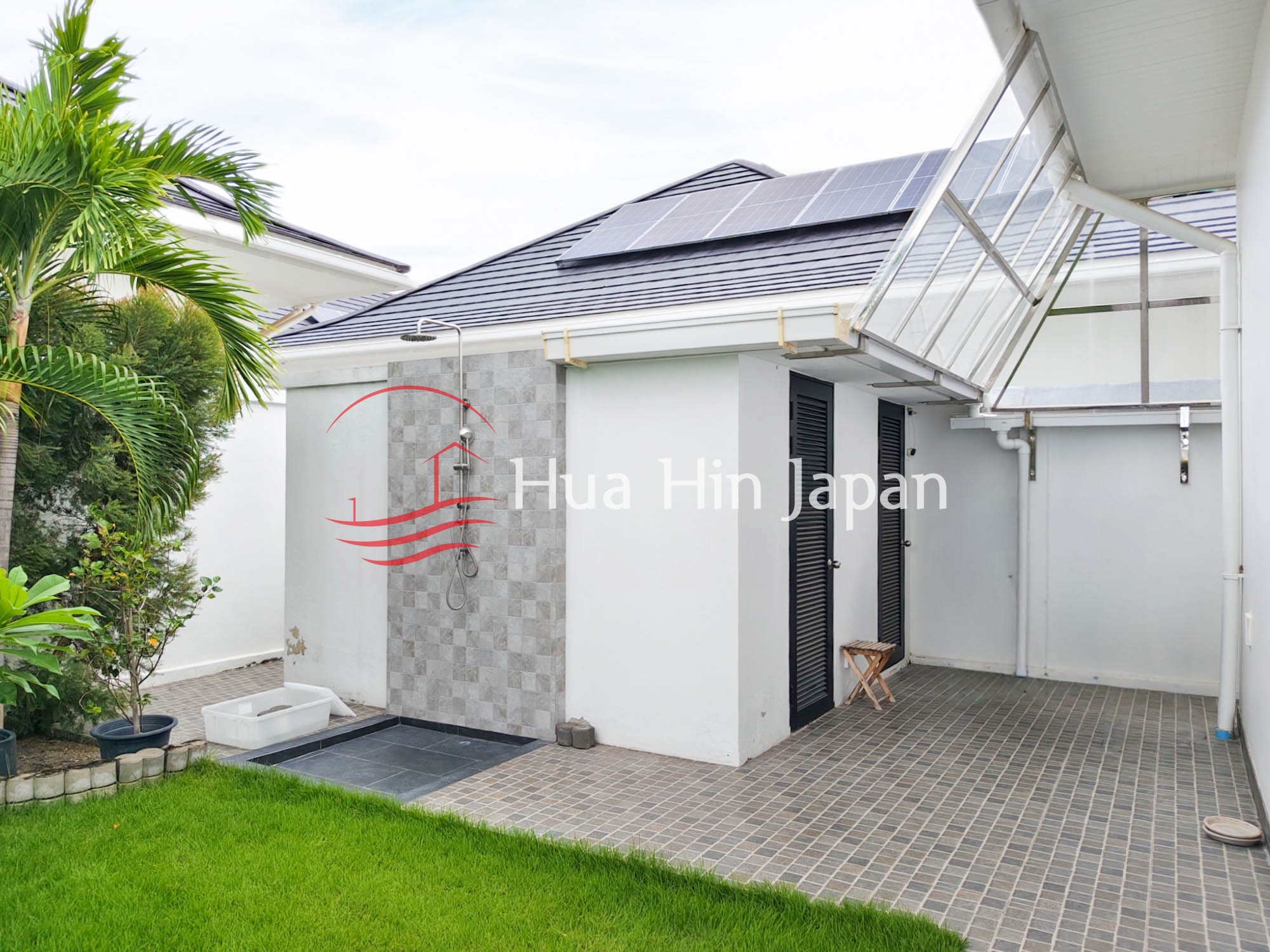 Modern house exterior with rooftop solar panels, outdoor shower, covered parking area, and green lawn