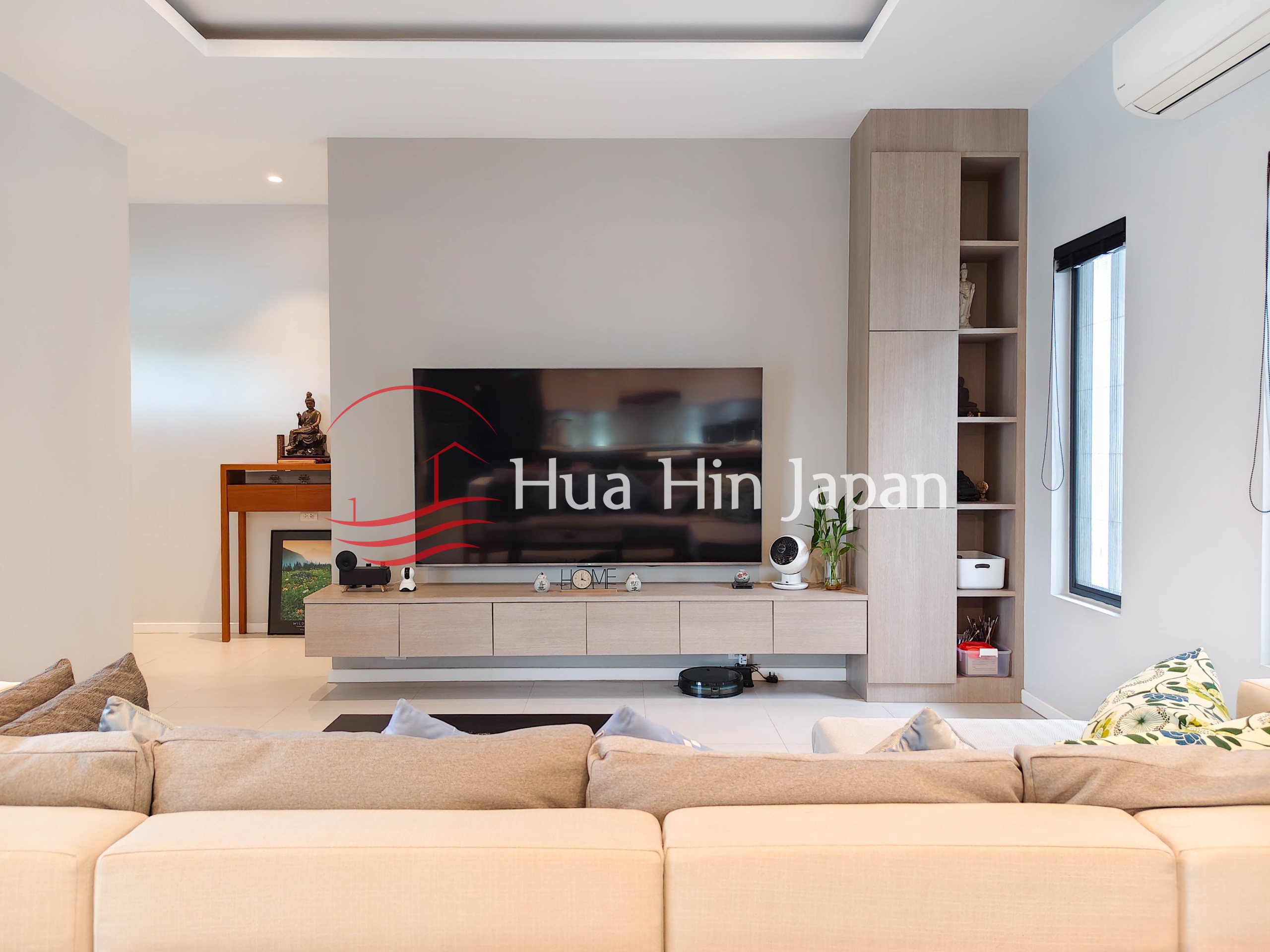 Modern living room with large TV, built-in wooden storage, sectional sofa, and air conditioning