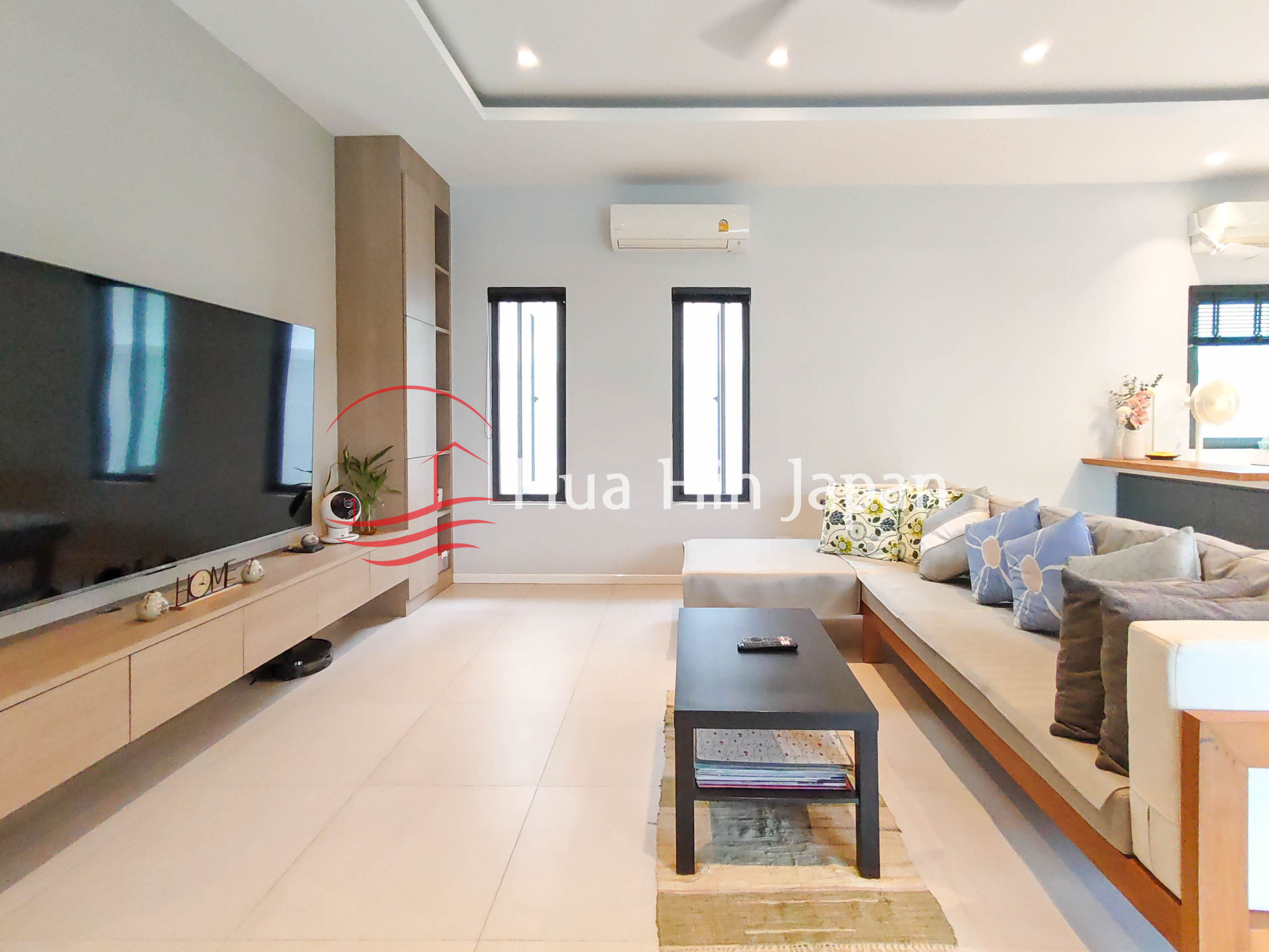 Modern living room with a large TV, cream sectional sofa, black coffee table, and minimalist built-in storage