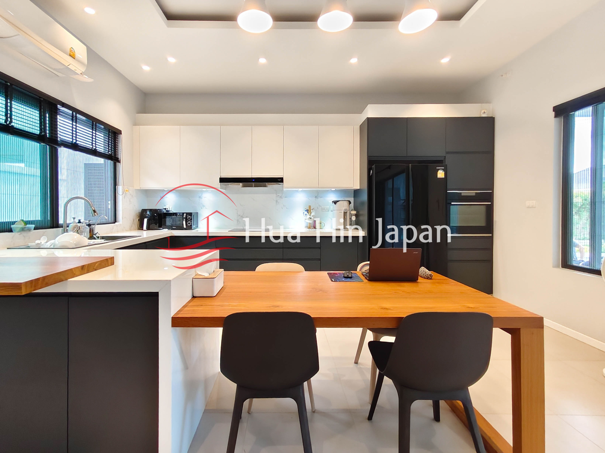 Modern open-plan kitchen and dining area with black and white cabinets, wooden dining table, appliances and large windows