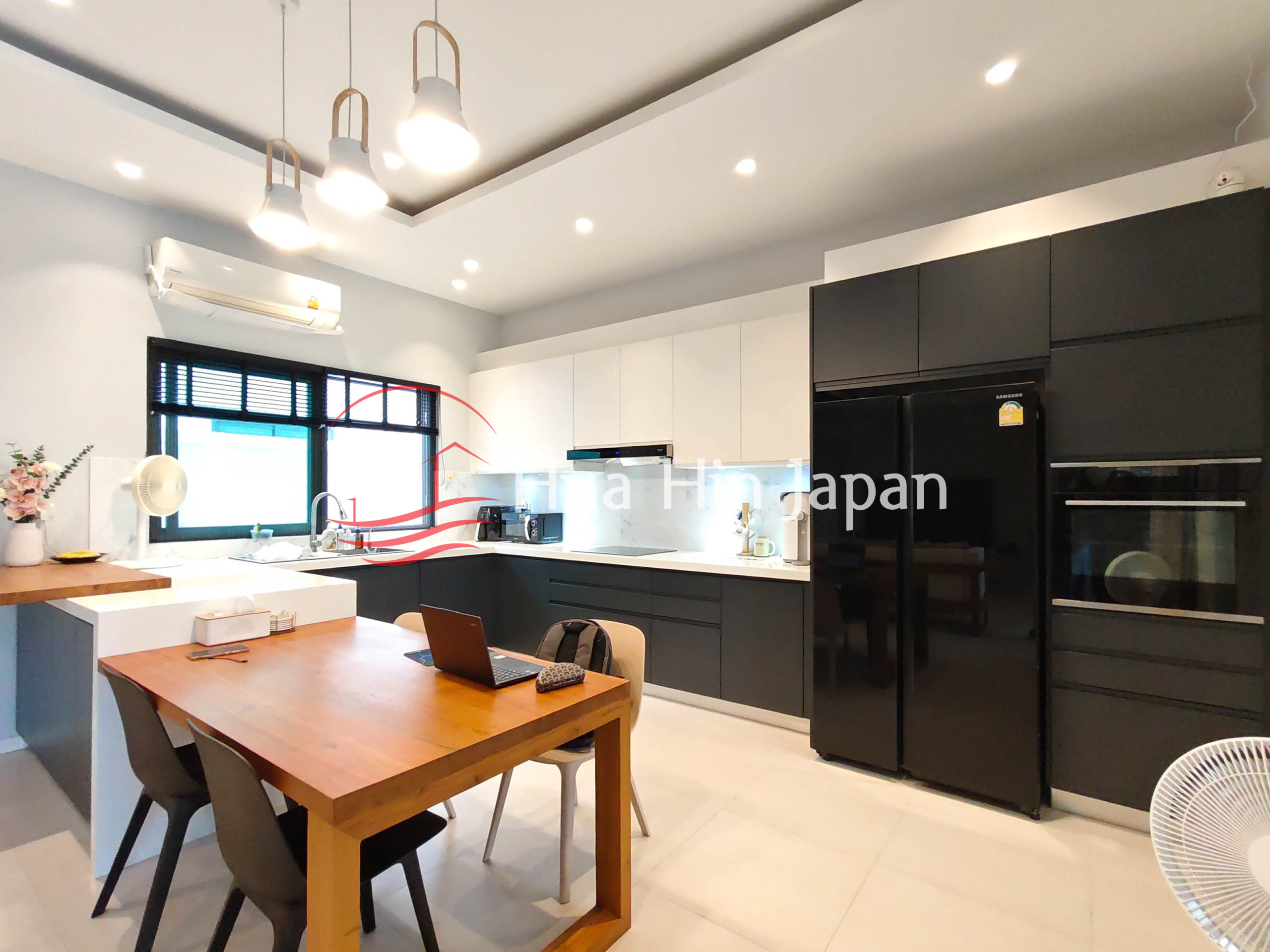 Modern kitchen and dining area with black and white cabinets, large refrigerator and wooden dining table