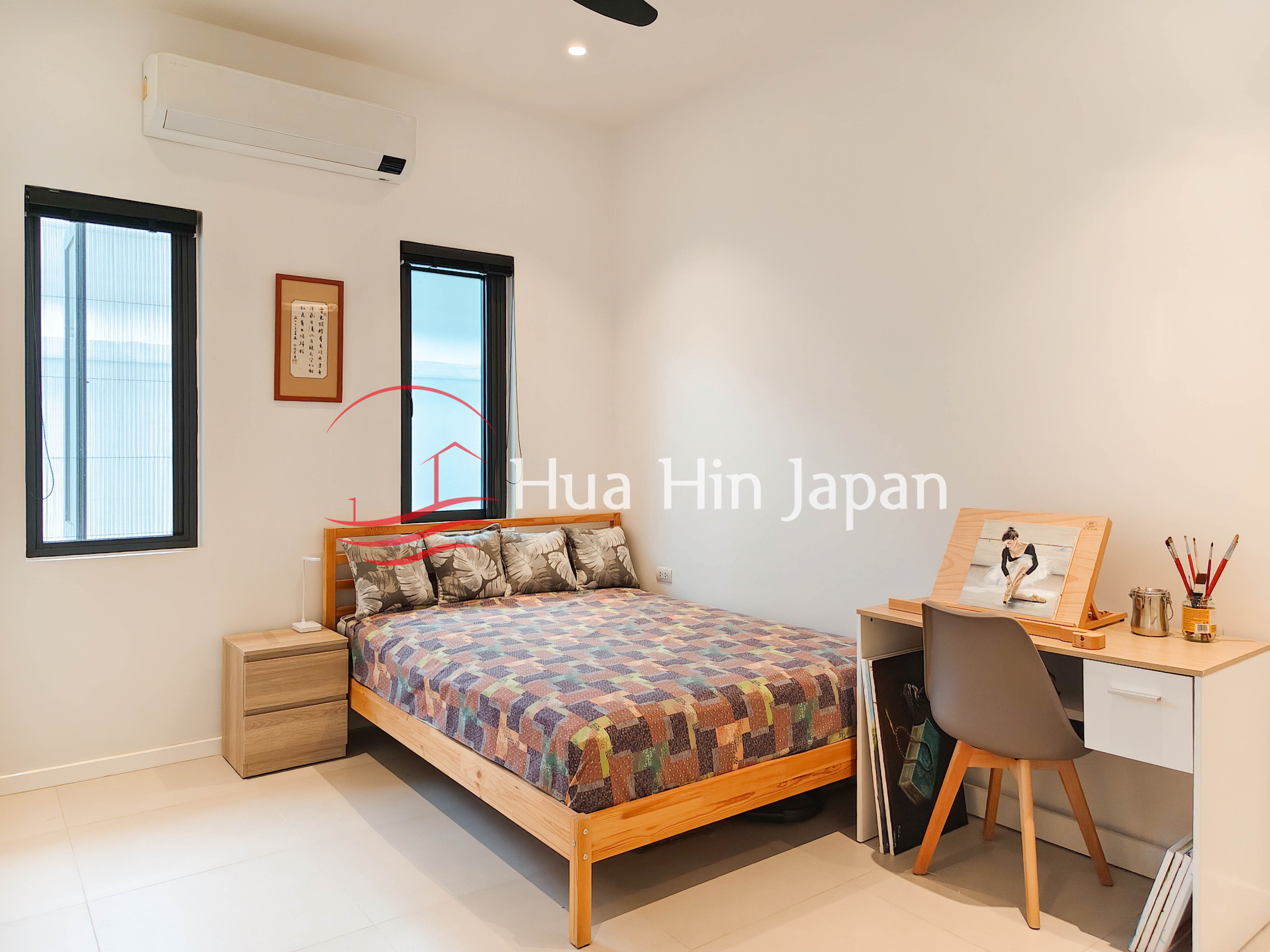 Bright bedroom with wooden bed, patterned bedding, desk, easel and air conditioner