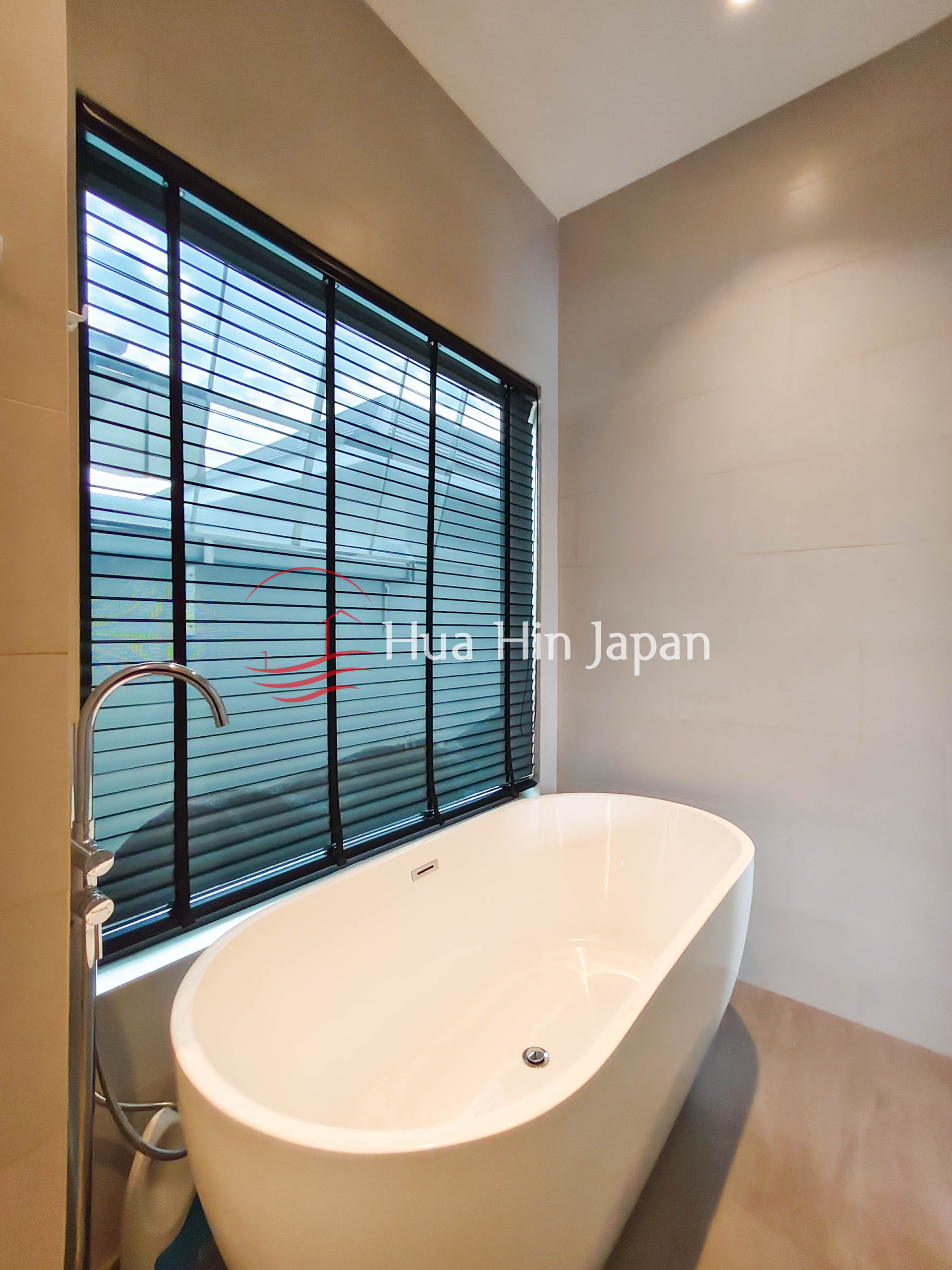 Freestanding white bathtub beside a large window with blinds