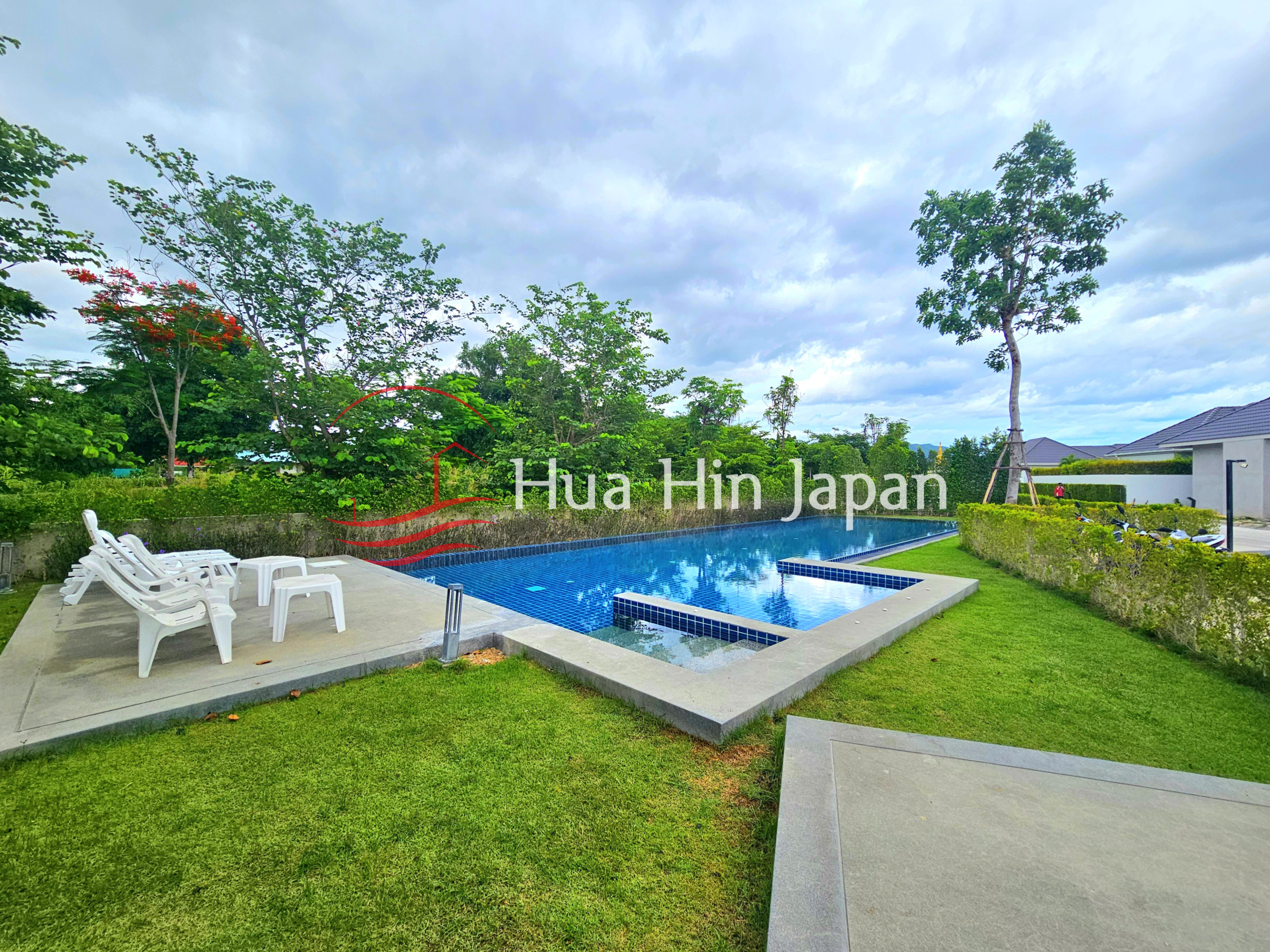Private outdoor swimming pool surrounded by a manicured lawn, trees, hedges, and white sun loungers