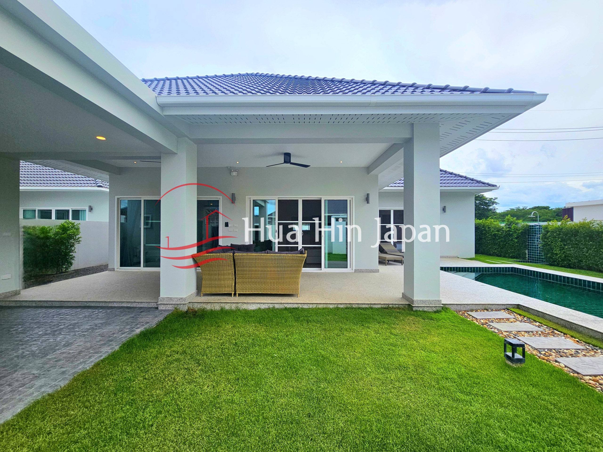 Modern villa with covered outdoor seating area, manicured lawn, private swimming pool, and large glass doors