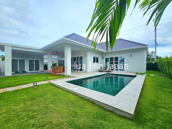 Modern single-story villa with a private tiled swimming pool, spacious green lawn, covered patio, and tropical landscaping