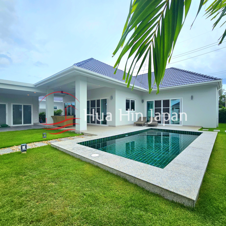 Modern single-story villa with a private tiled swimming pool, spacious green lawn, covered patio, and tropical landscaping