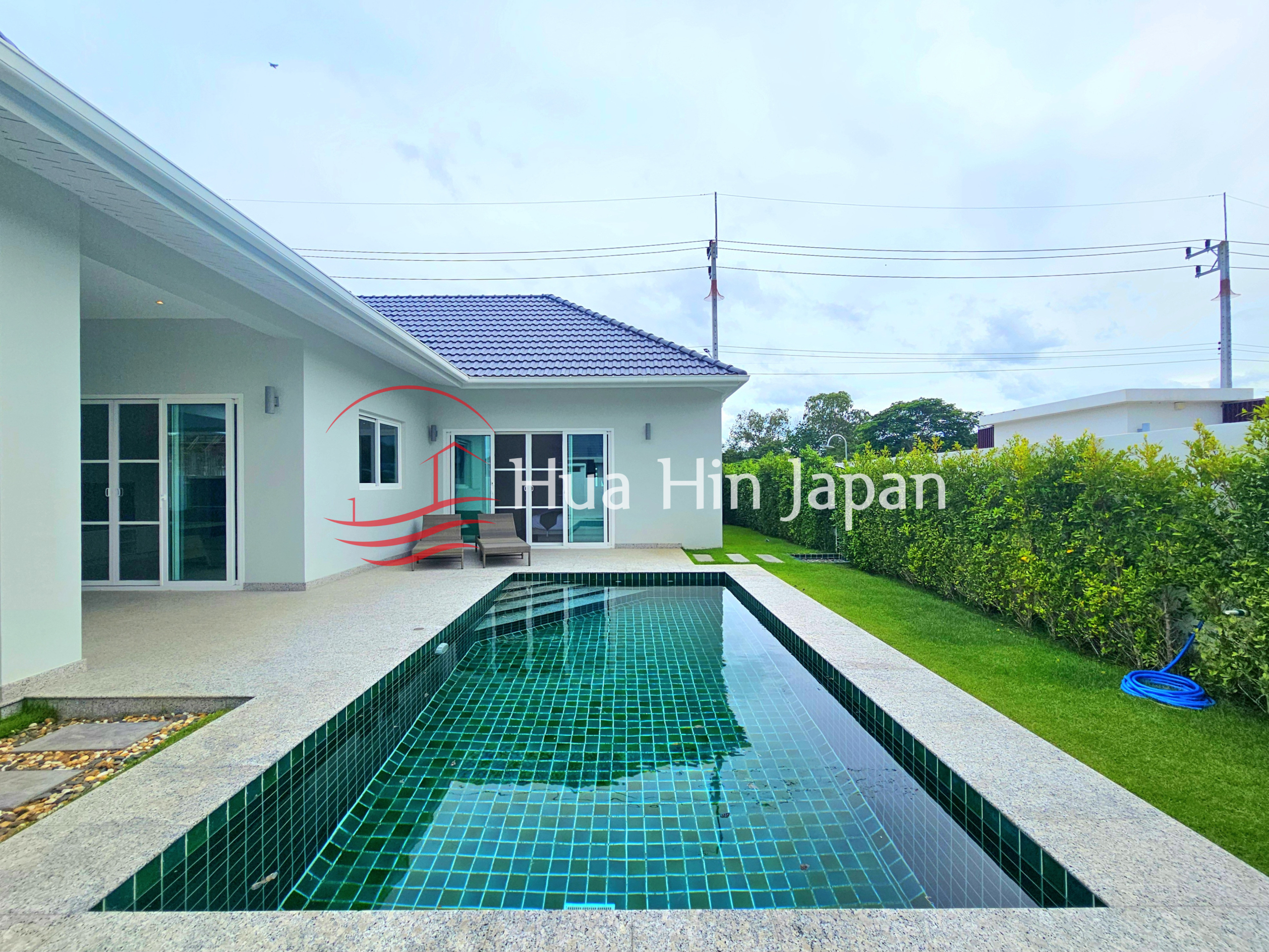 Private rectangular swimming pool beside a modern single-story villa with a landscaped garden and trimmed hedges