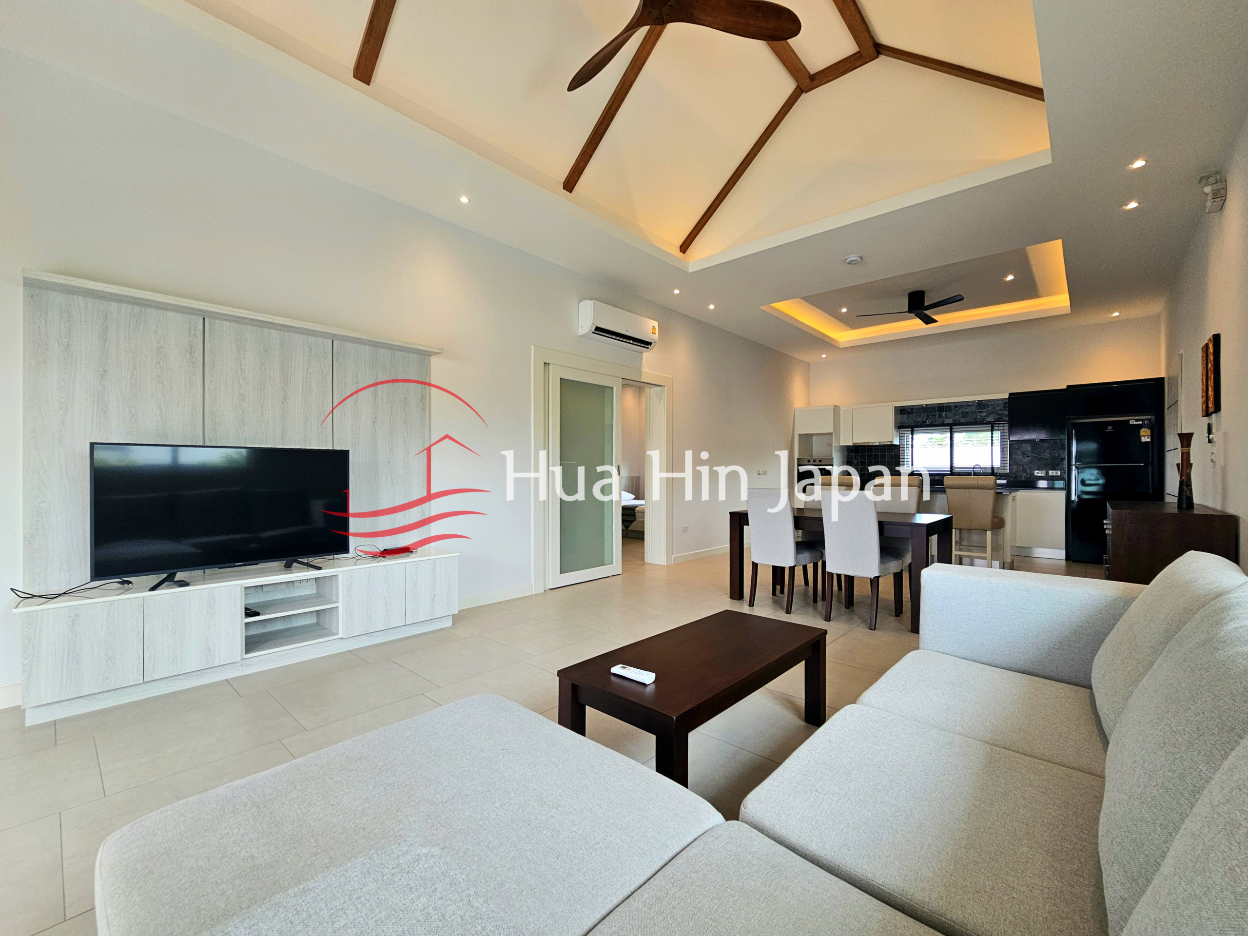 Bright modern living room with a large sectional sofa, TV, coffee table, dining area, and open kitchen
