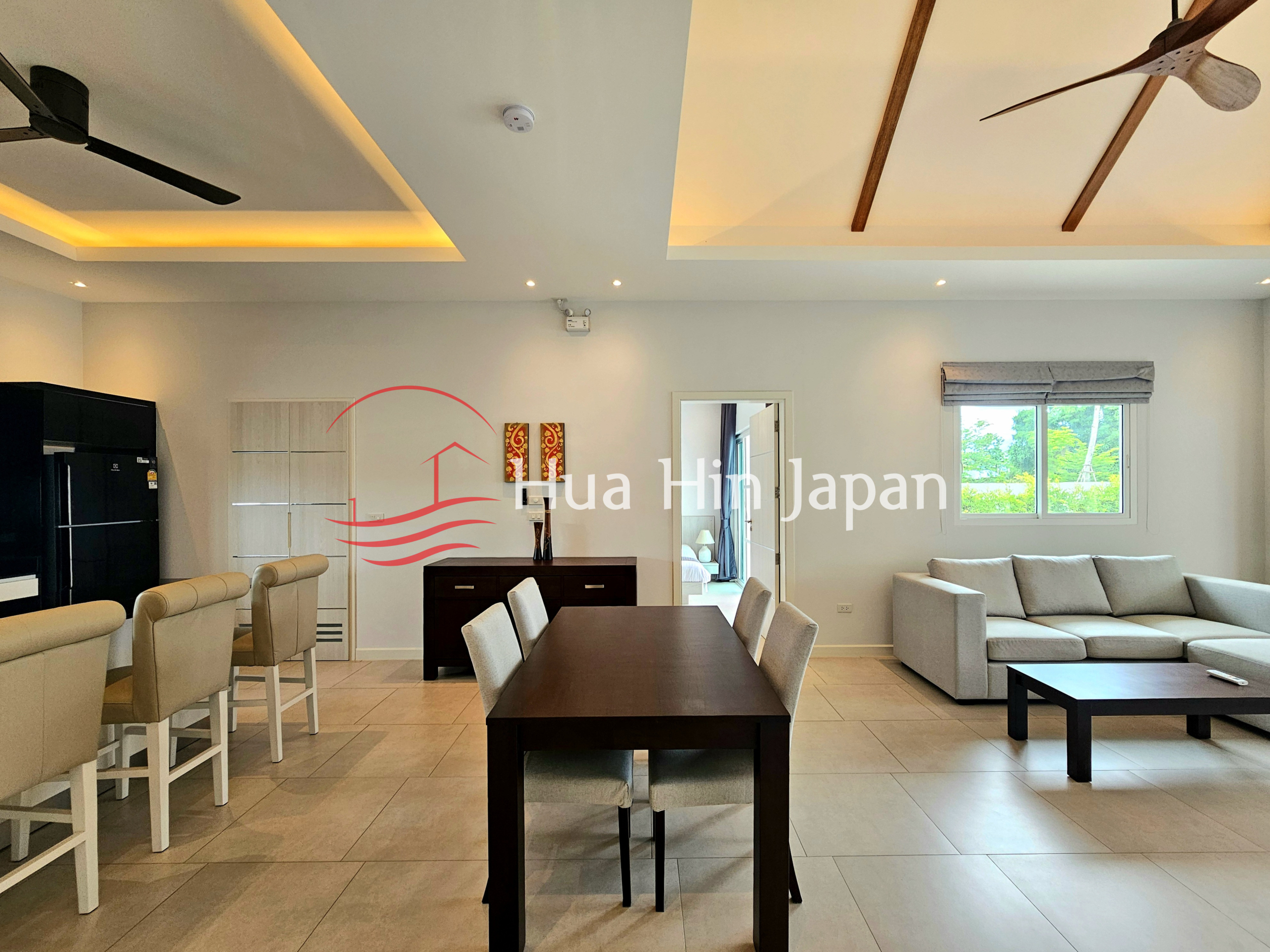 Open-plan dining and living area with a dark wood dining table, upholstered chairs, sofa, coffee table, and kitchen bar