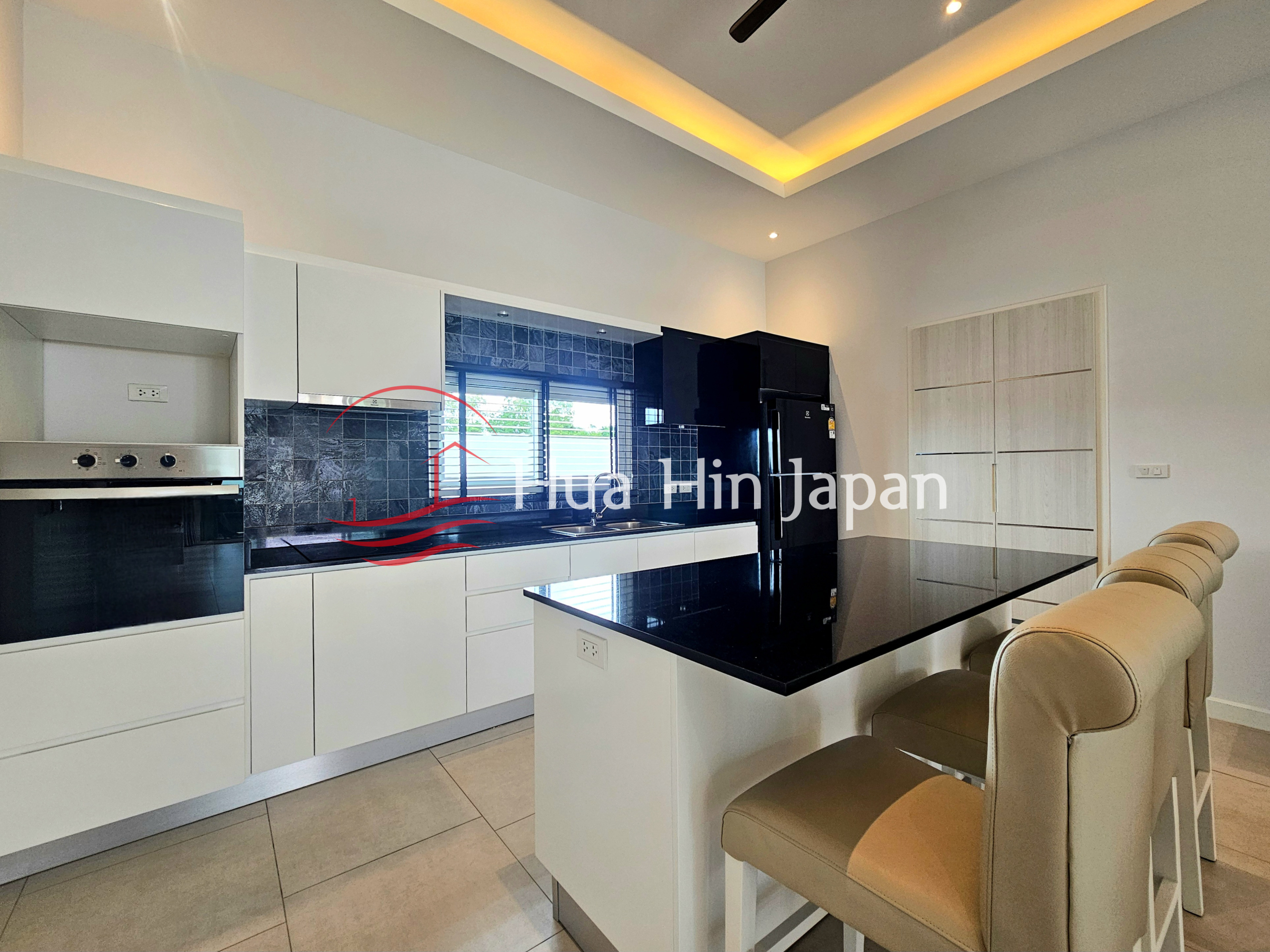 Modern white kitchen with black countertop island, built-in oven, refrigerator, and bar stools