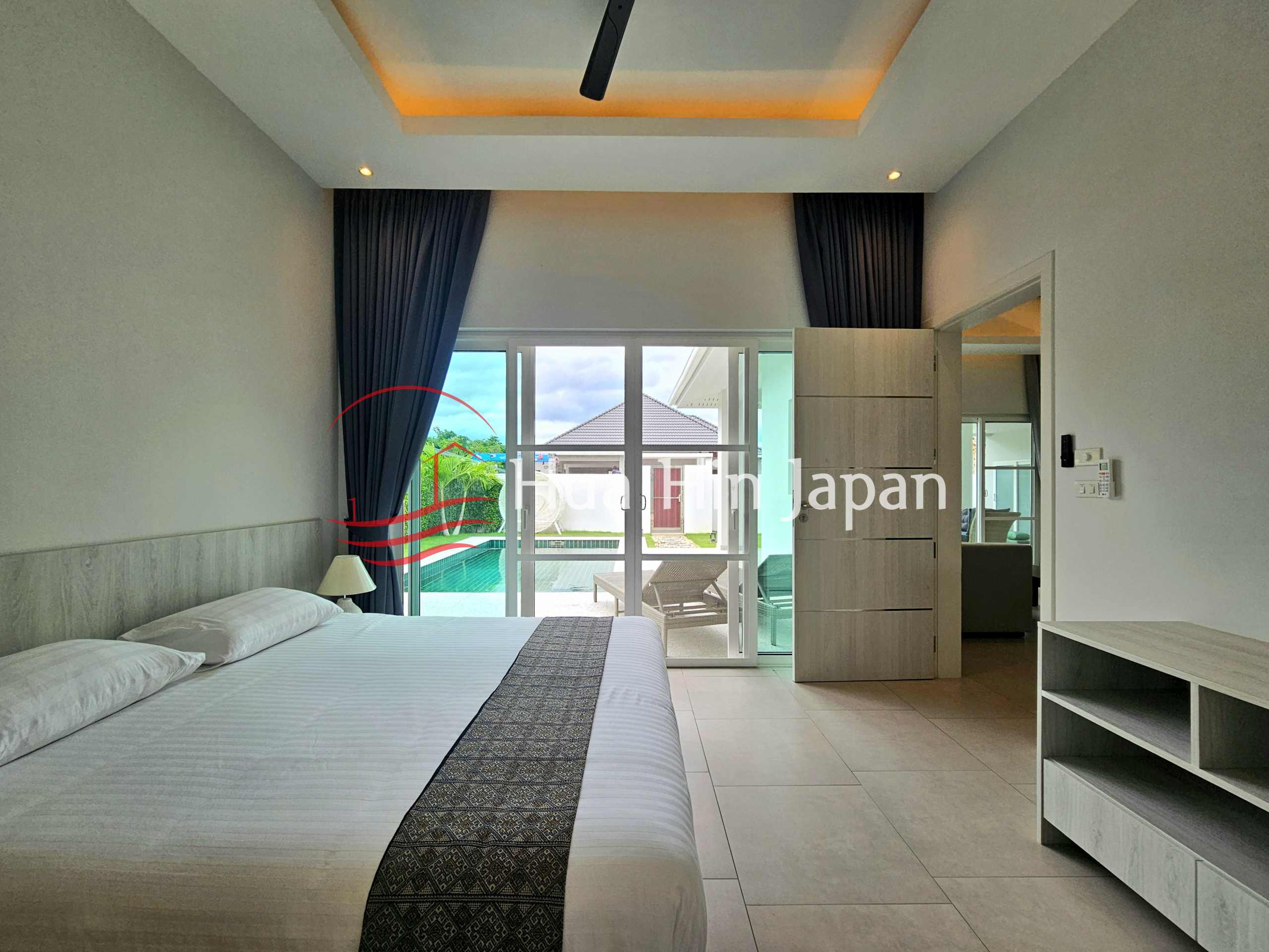 Modern bedroom with a large bed, dark curtains, built-in wood cabinetry, and sliding glass doors overlooking a swimming pool