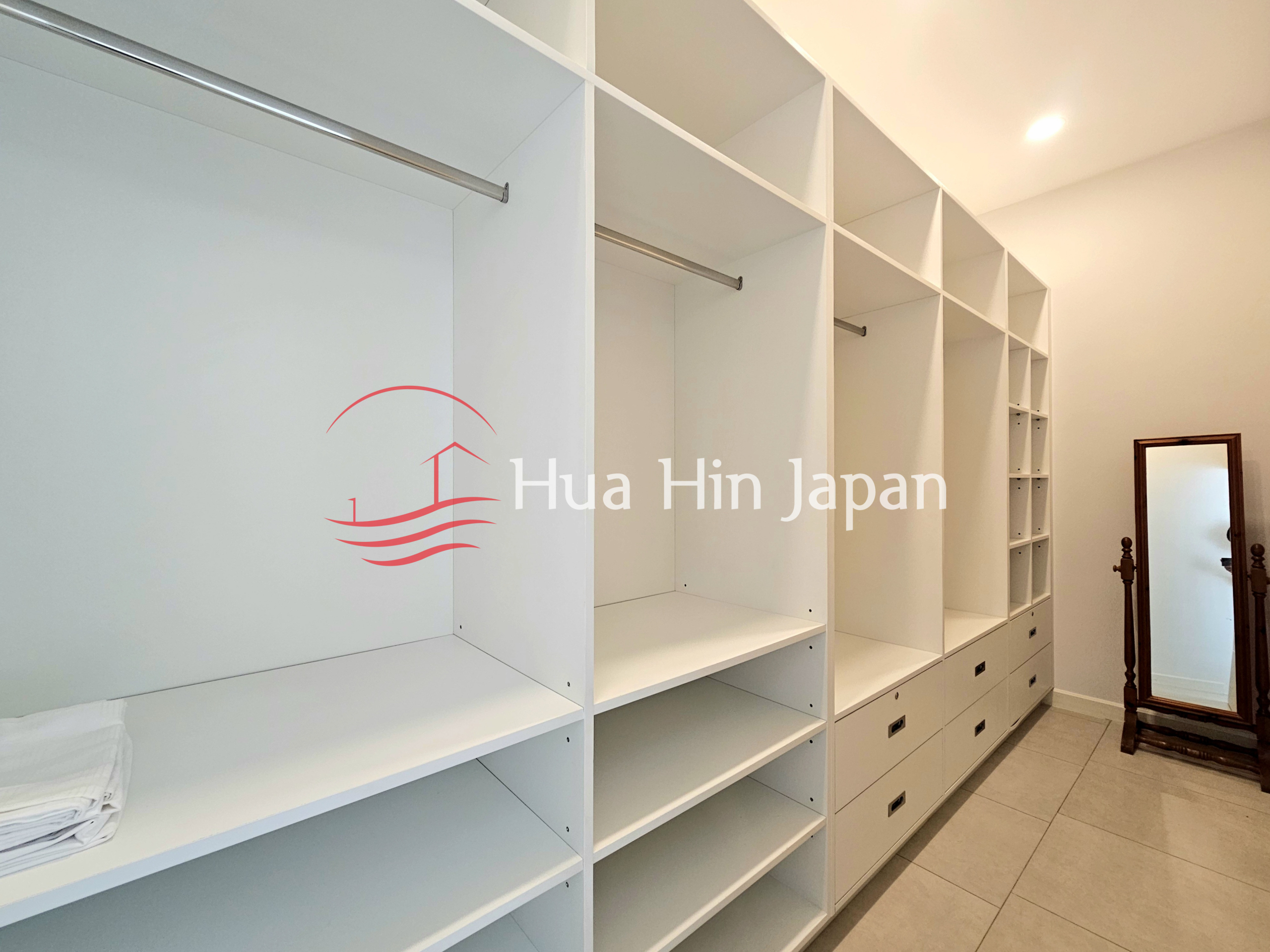 Spacious built-in walk-in wardrobe with white shelving, hanging rails, drawers, and full-length mirror