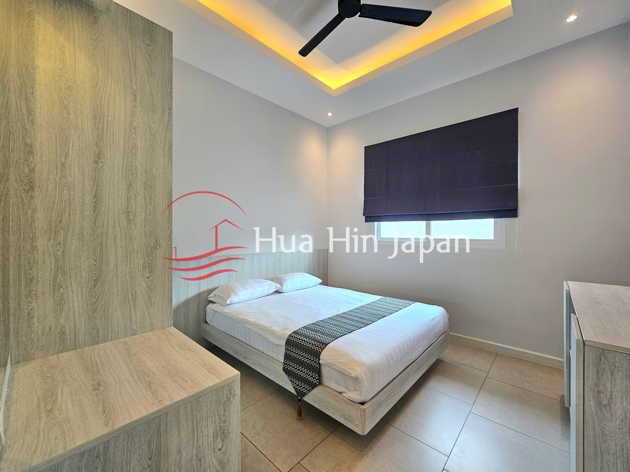 Modern bedroom with a double bed, wood-finish built-in storage, roller blind, and warm ceiling lighting