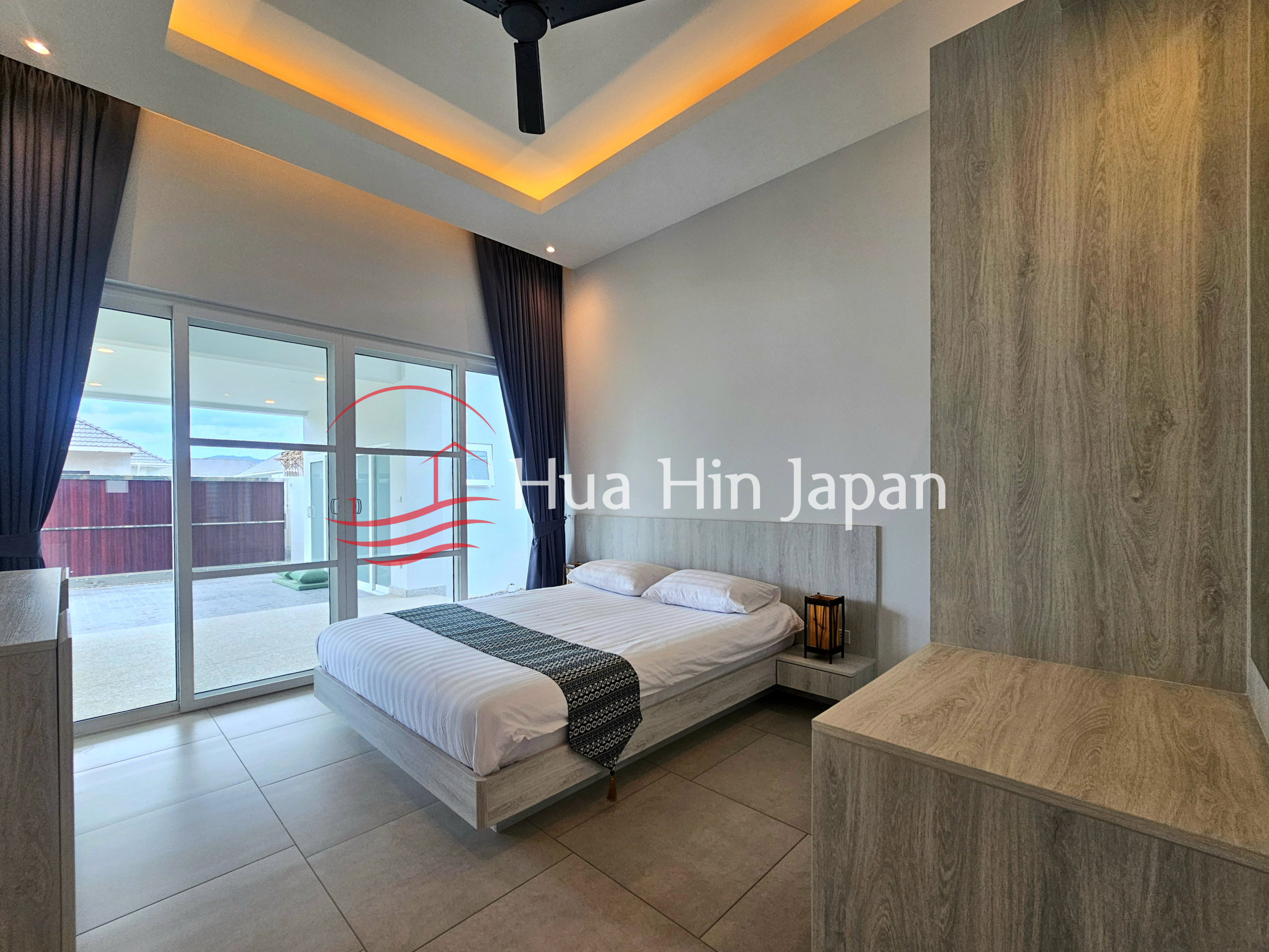 Modern bedroom with a large bed, wood-paneled wardrobe, sliding glass doors, and warm ceiling lighting