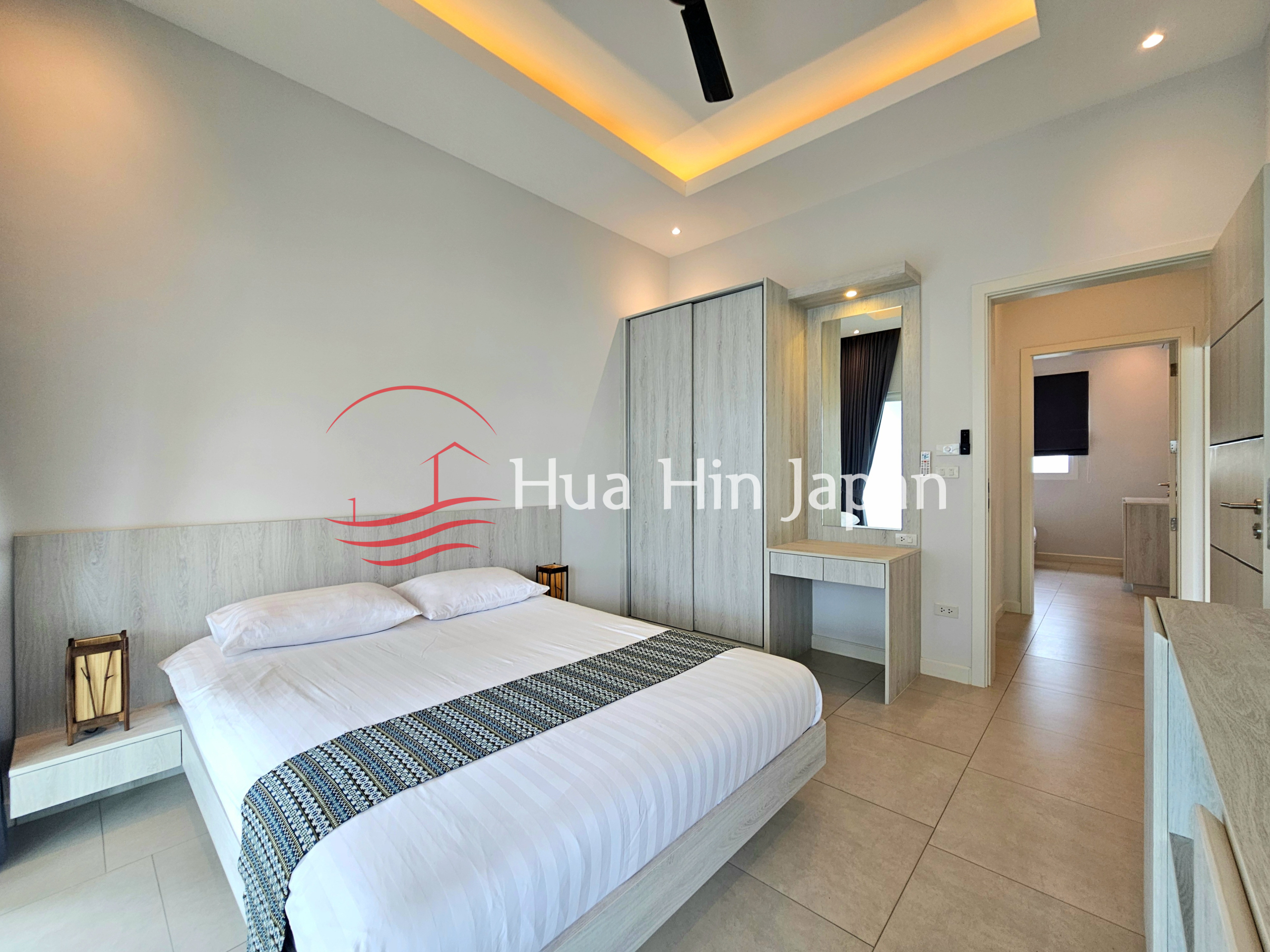 Modern bedroom with a large bed, built-in wardrobe, dressing table, and warm ceiling lighting