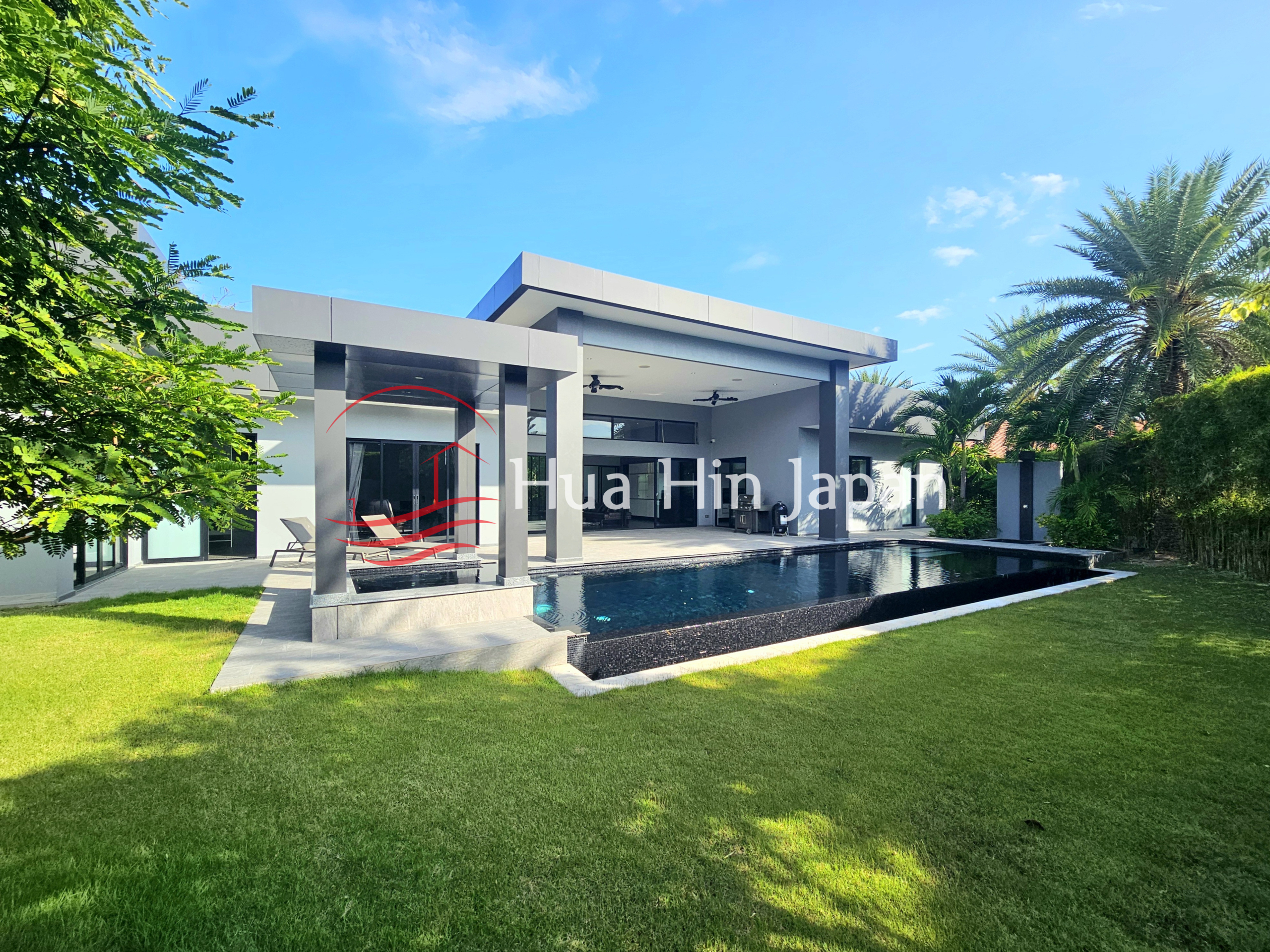Modern luxury villa with a private swimming pool, spacious lawn, and tropical landscaping