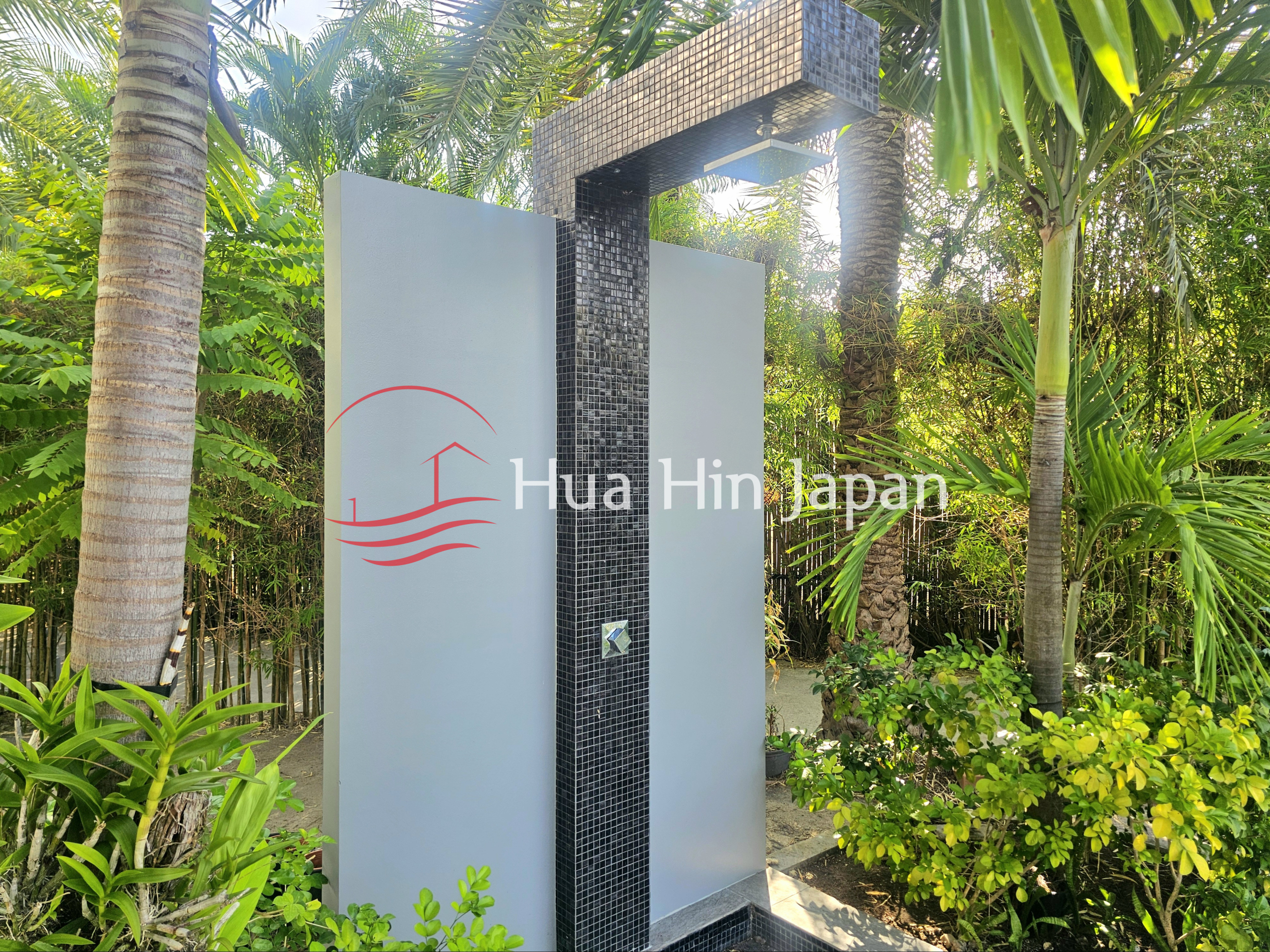 Outdoor shower with black mosaic tile column surrounded by lush tropical greenery