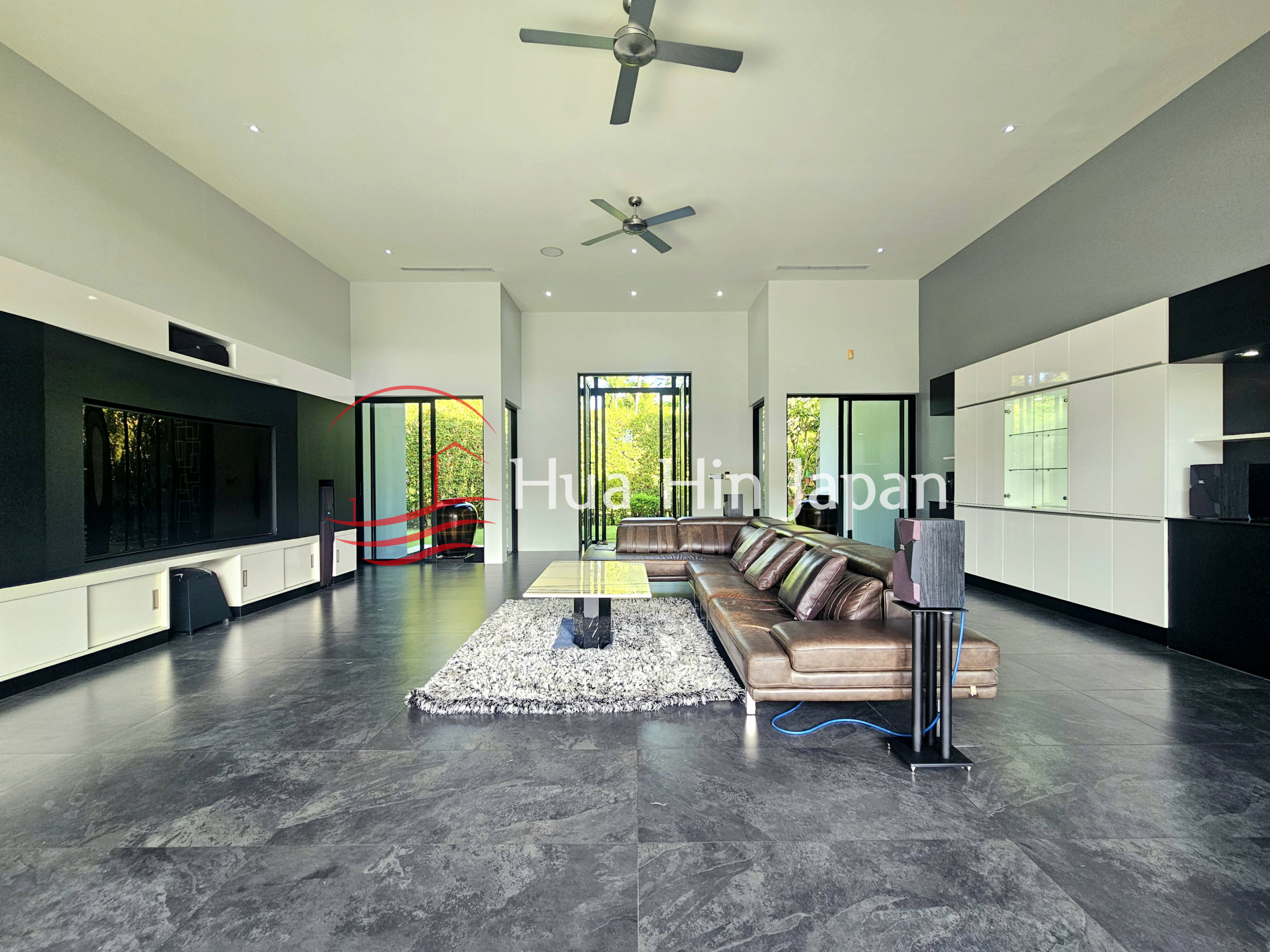 Spacious modern living room with a large brown sectional sofa, built-in TV wall, white cabinetry, and garden views