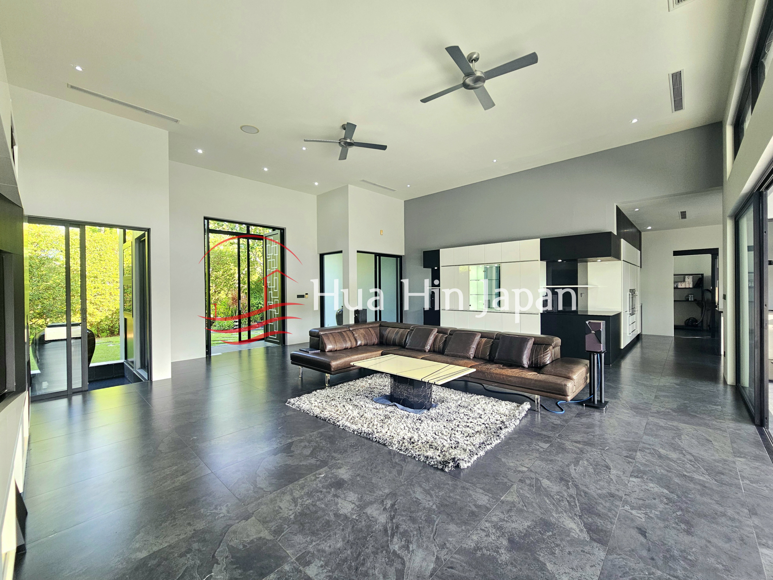 Spacious modern living room with a large sectional sofa, dark flooring, white cabinetry, and garden views