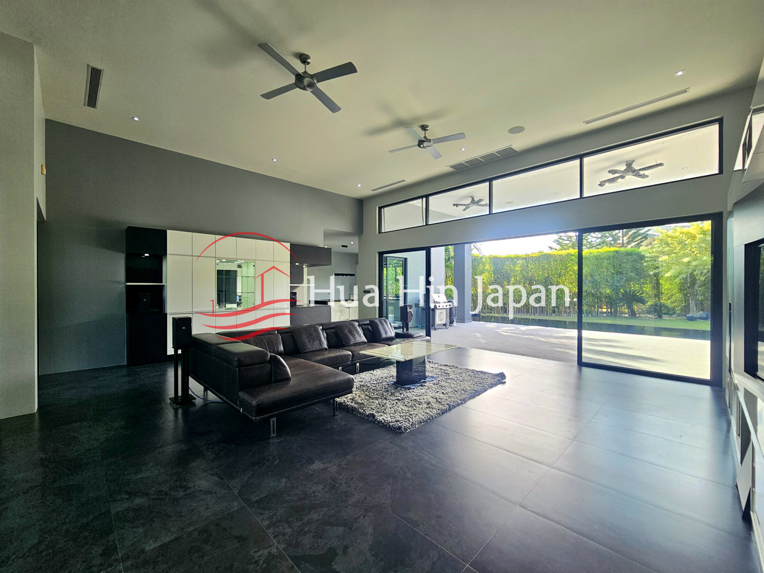 Spacious modern living room with black sectional sofa, glass coffee table, and large sliding doors overlooking the garden