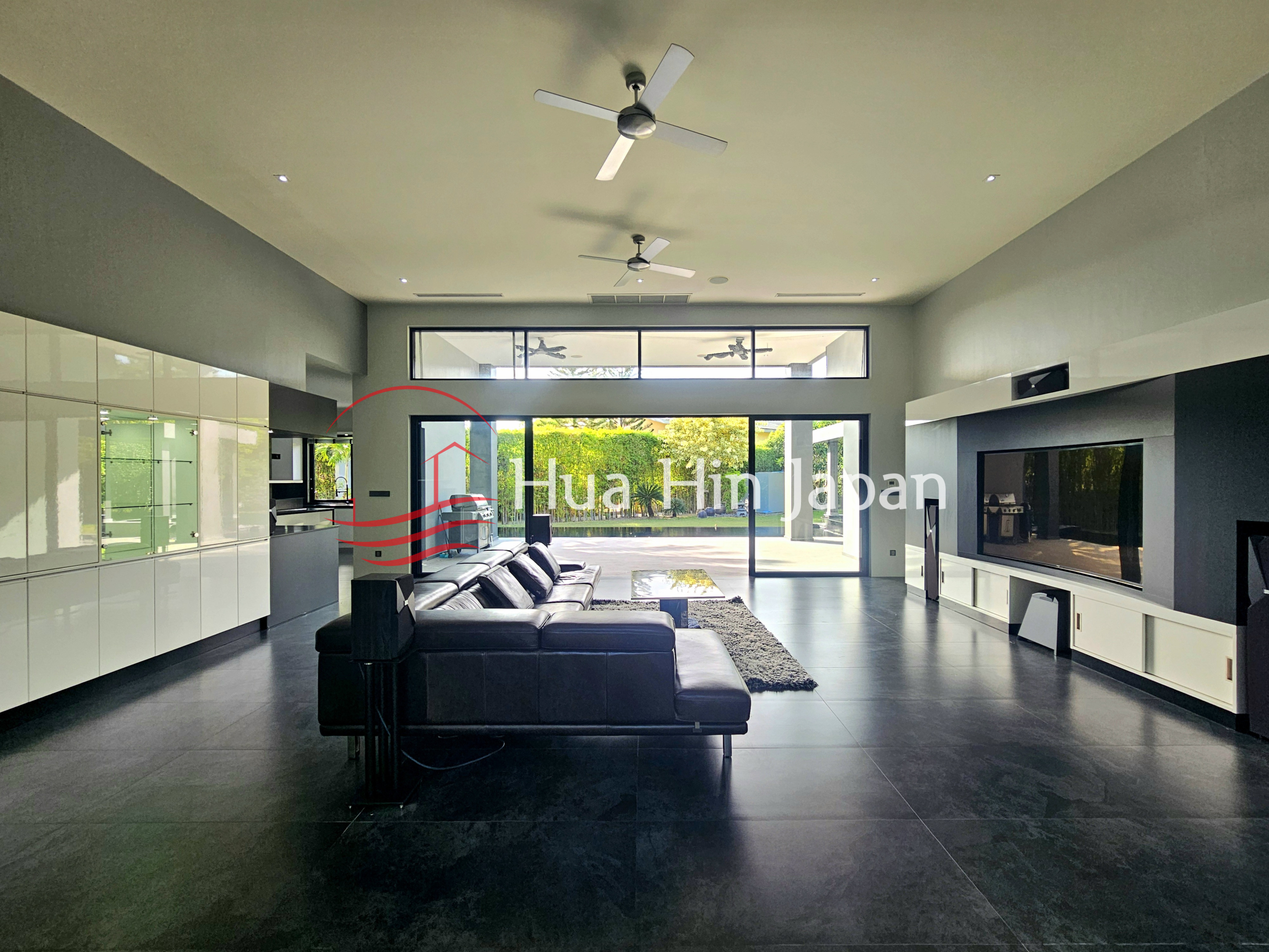 Spacious modern living room with black leather sectional sofa, large TV wall, and glass doors opening to the garden