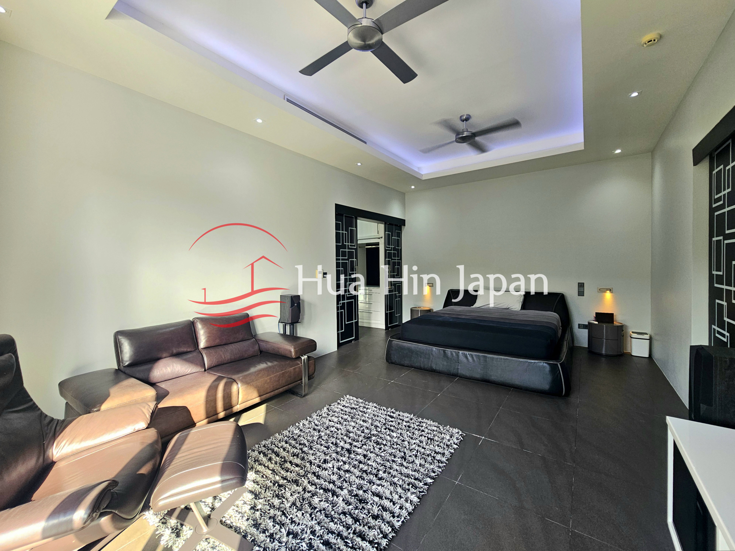 Spacious modern bedroom with a large bed, leather sofa, recliner, ceiling fans, and dark tiled flooring