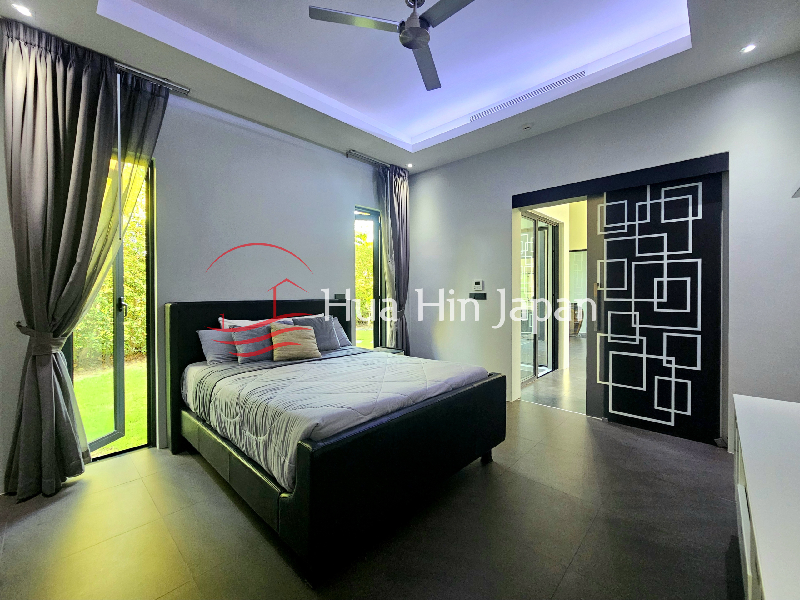 Modern bedroom with a black upholstered bed, gray curtains, ceiling fan, and decorative geometric glass doorway