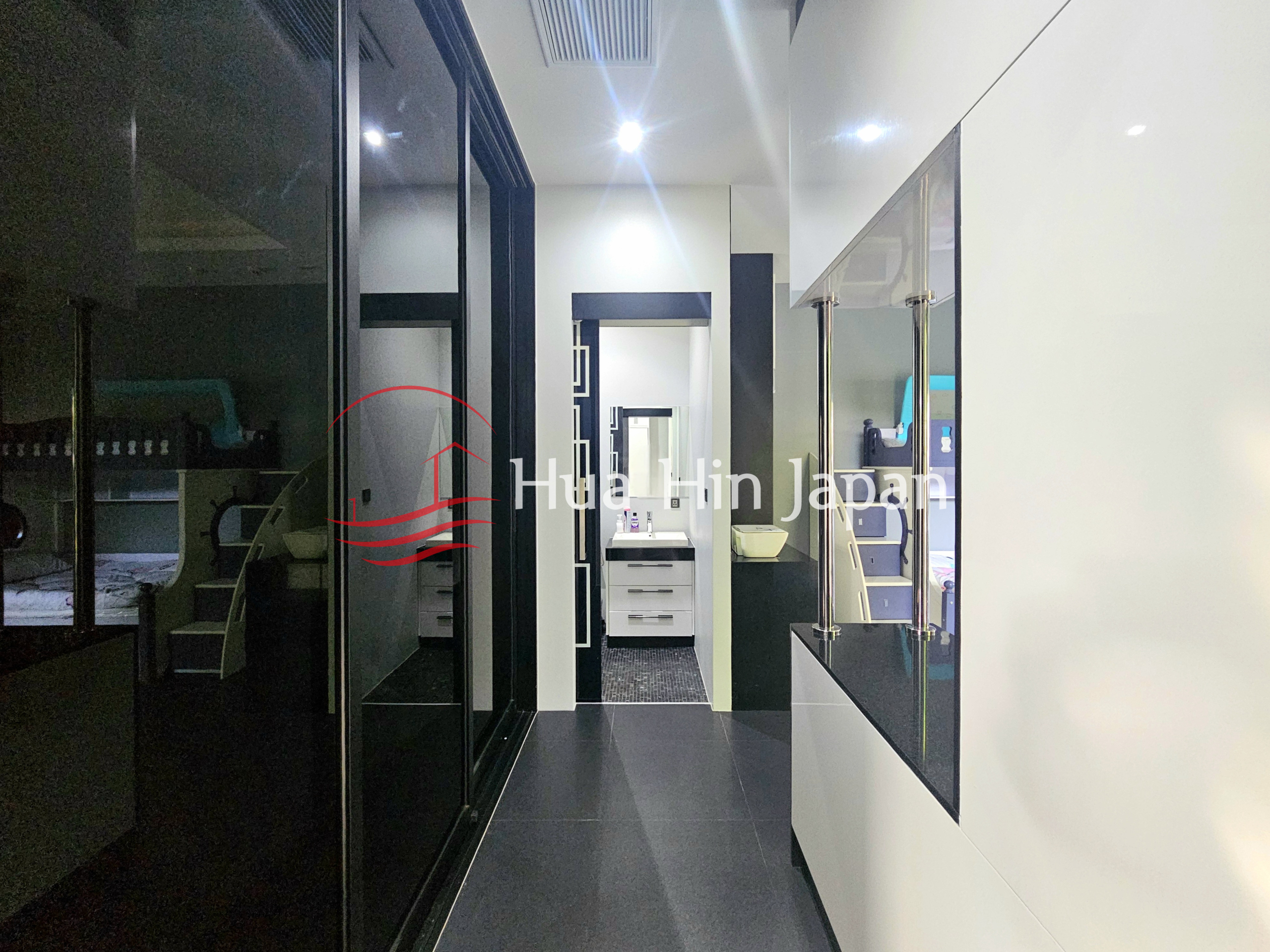 Modern hallway with black tiled flooring, glass doors, built-in white cabinetry, and views into a bedroom and bathroom