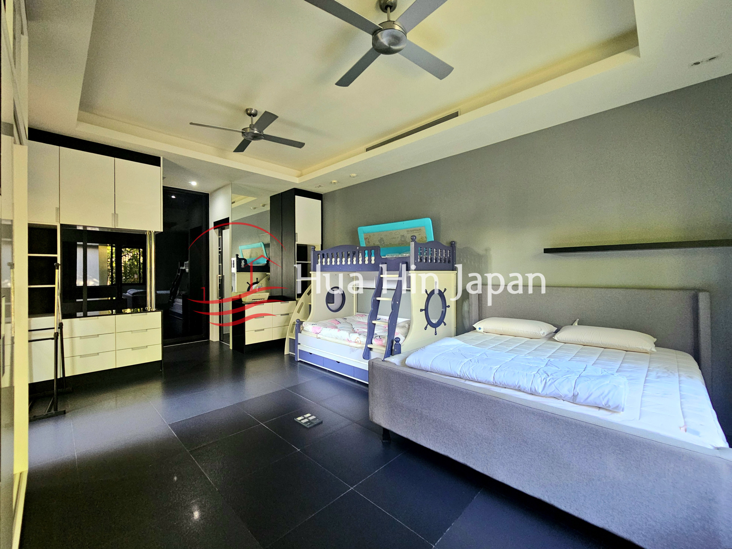 Spacious modern bedroom with a double bed, children’s nautical-themed bunk bed, built-in white wardrobes, and ceiling fans