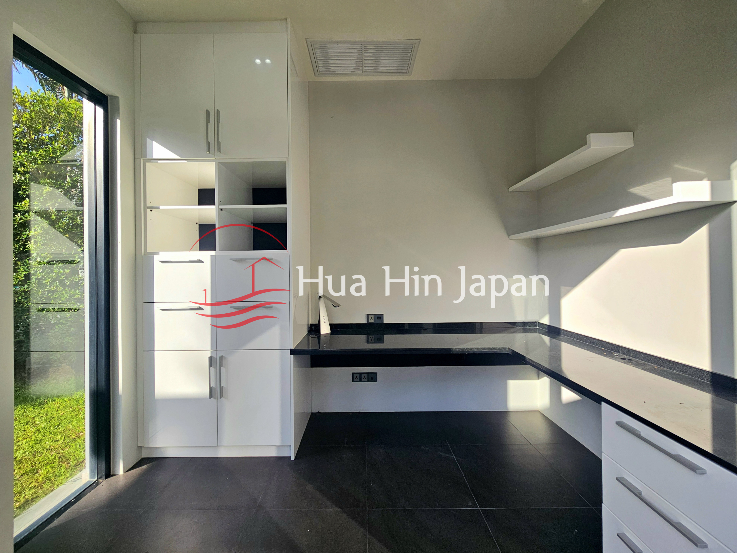 Modern home office with white built-in cabinets, black countertops, open shelving, and large glass door