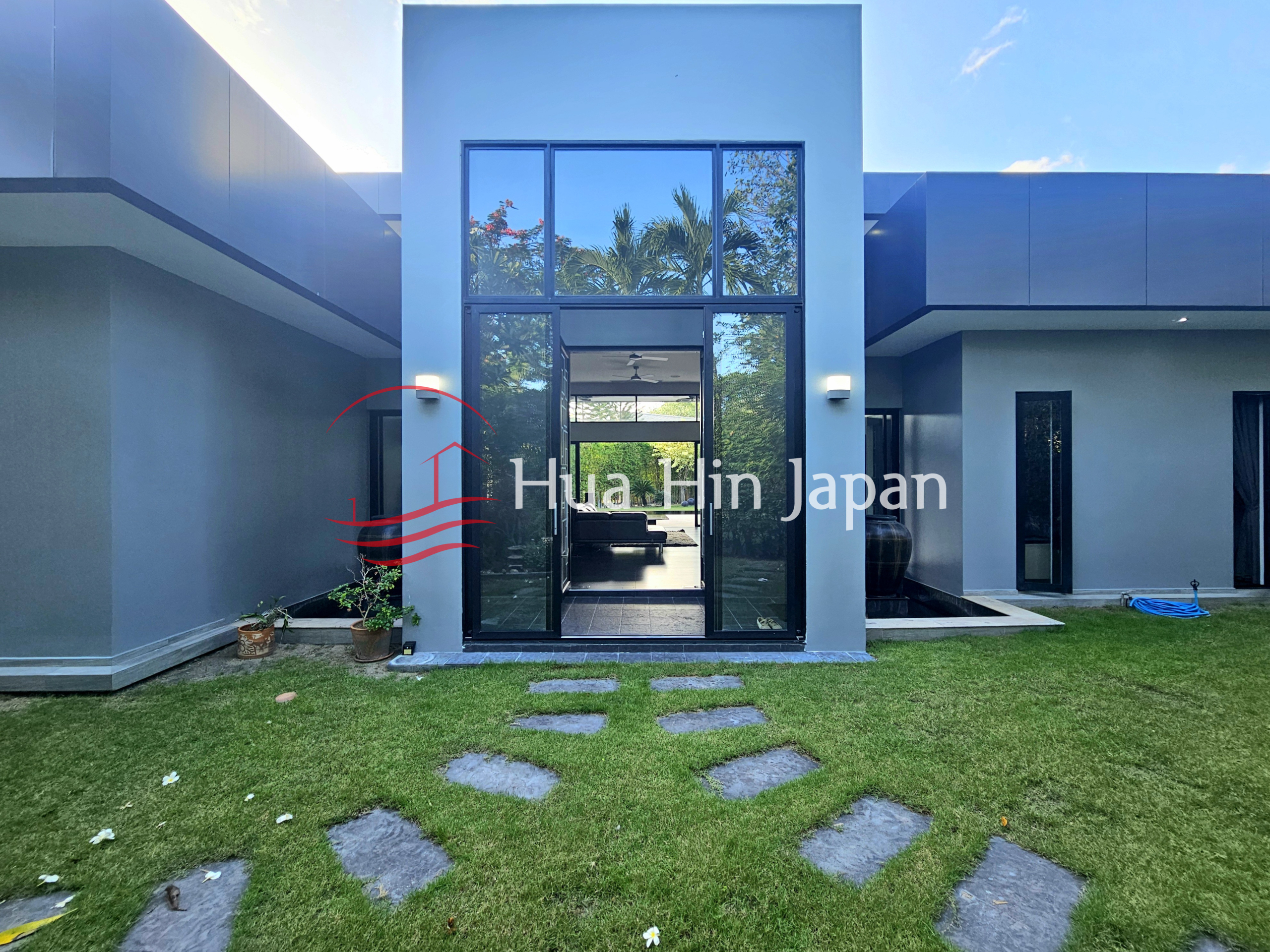 Modern villa exterior with a glass entrance, manicured lawn, stepping-stone pathway, and contemporary architectural design