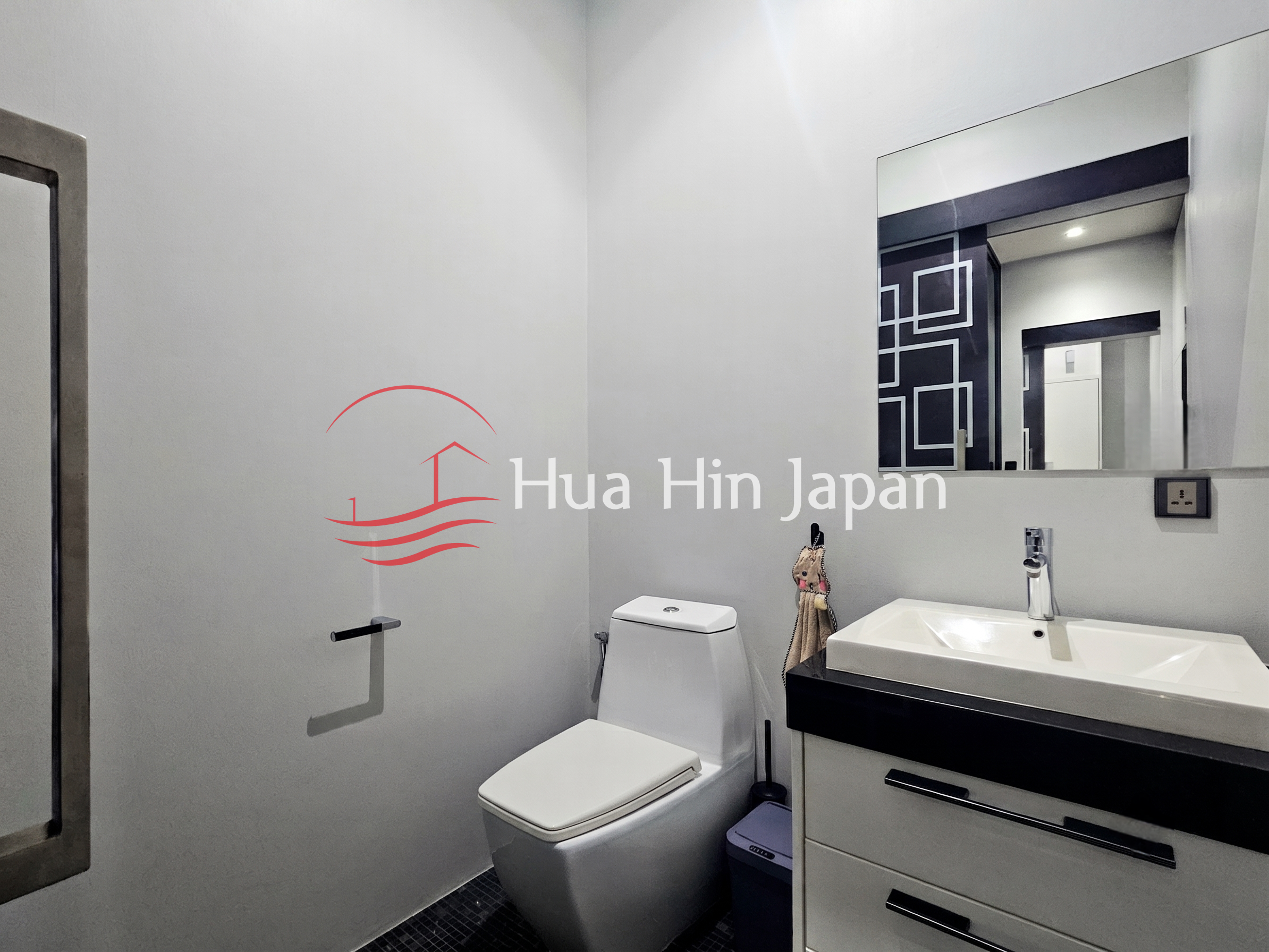 Modern bathroom with a white toilet, rectangular sink, black-and-white vanity, and large wall mirror