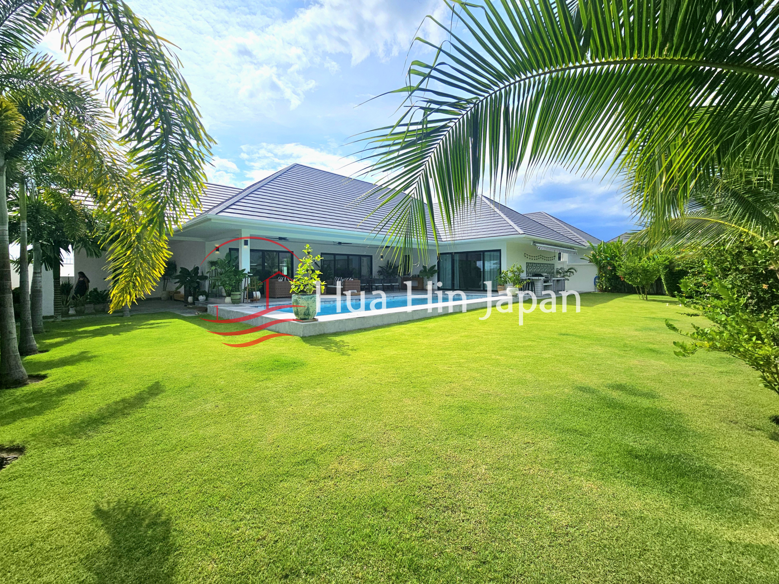 Modern tropical villa with a private pool, expansive green lawn, palm trees, and a covered outdoor living area