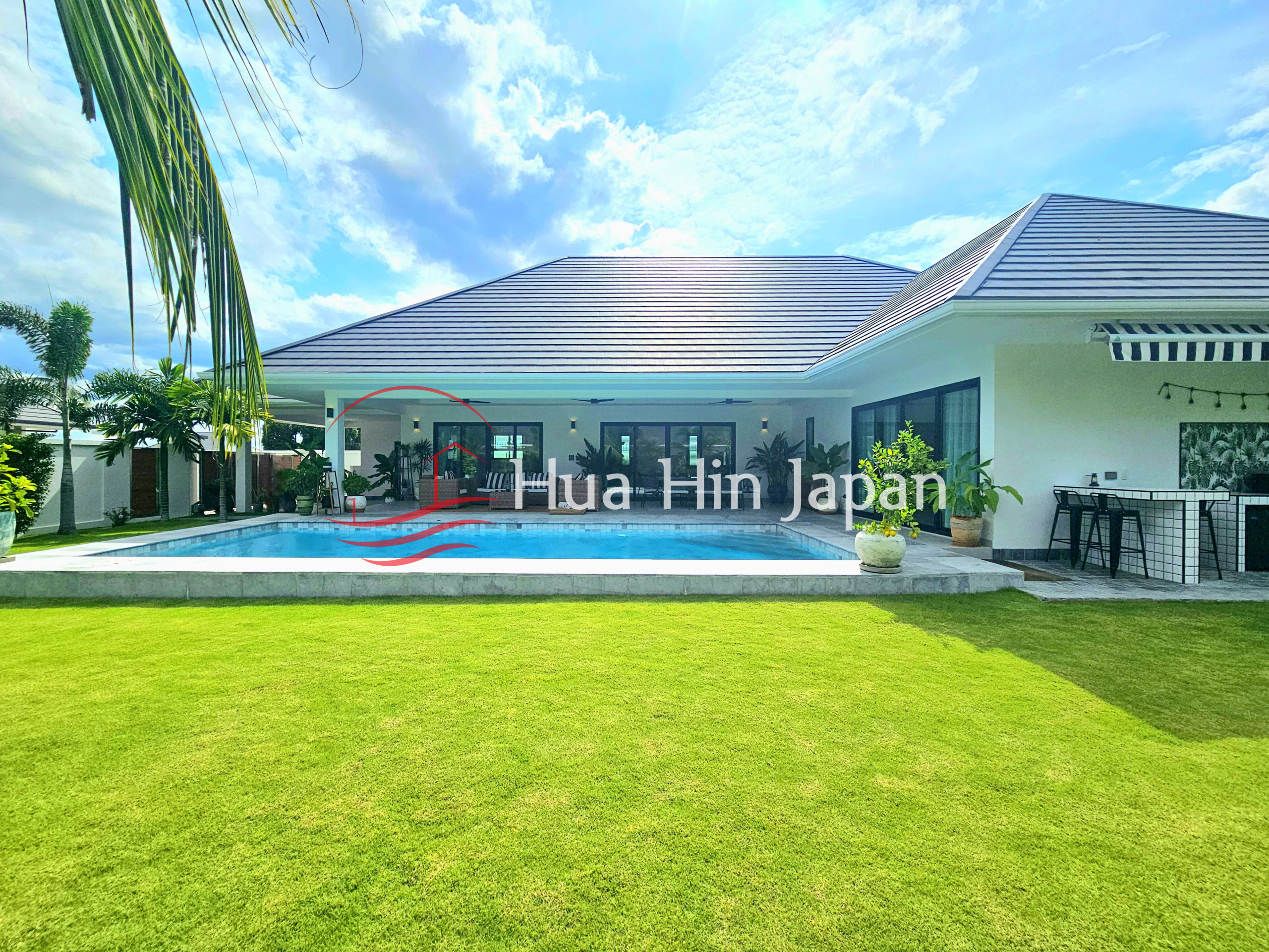 Modern villa with a private swimming pool, spacious green lawn, covered outdoor lounge, and tropical landscaping