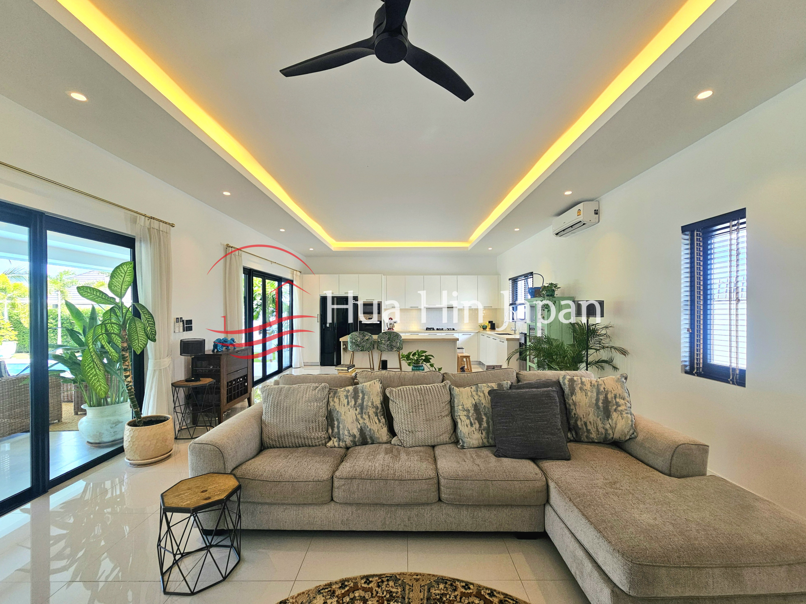 Spacious modern living room with a large sectional sofa, indoor plants, ceiling fan, and open-plan kitchen