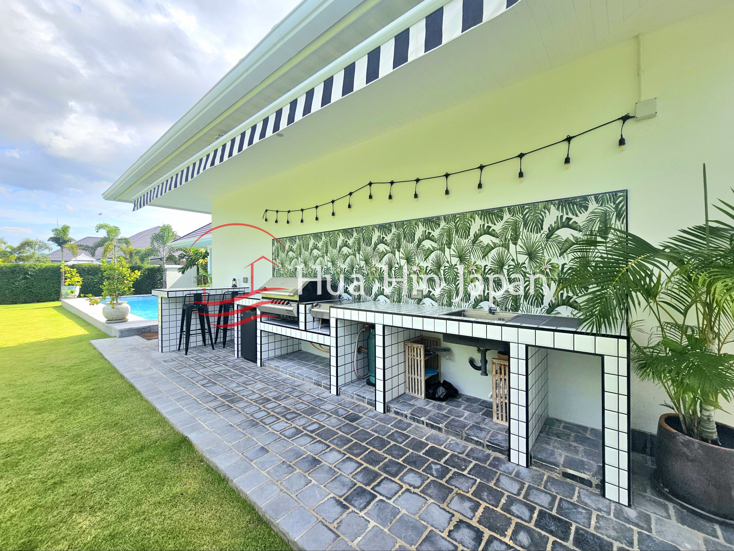 Outdoor kitchen and dining area beside a landscaped lawn and swimming pool